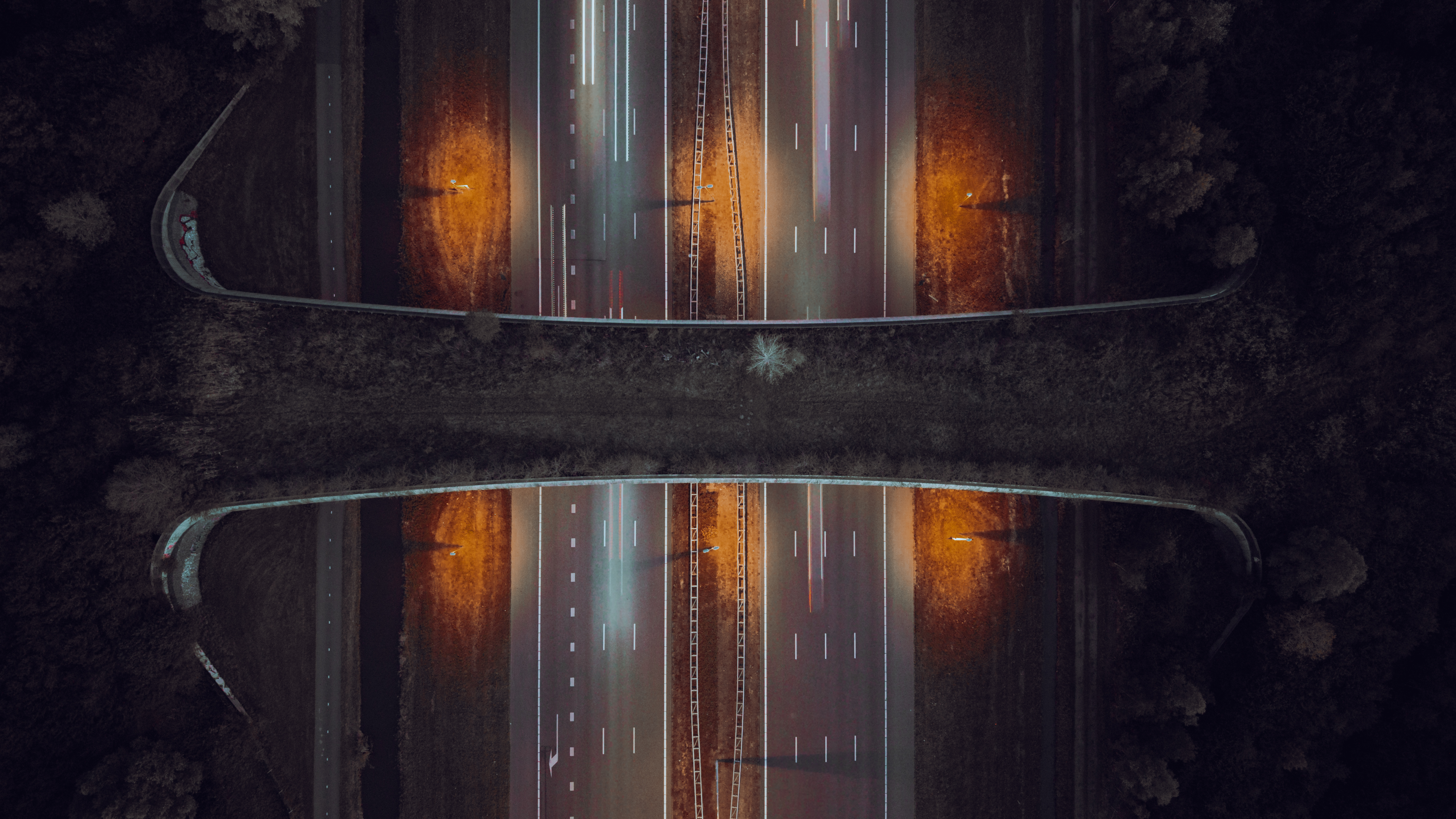 Vue aérienne nocturne d'une autoroute avec traînées lumineuses de voitures et pont au-dessus.