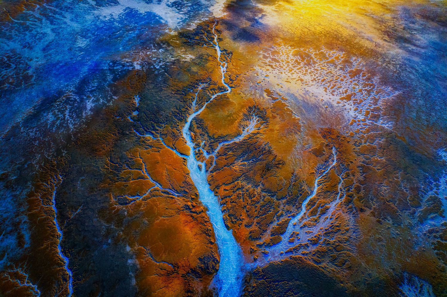 Vue aérienne colorée d’un fleuve serpentant à travers un paysage aux teintes bleu et ocre