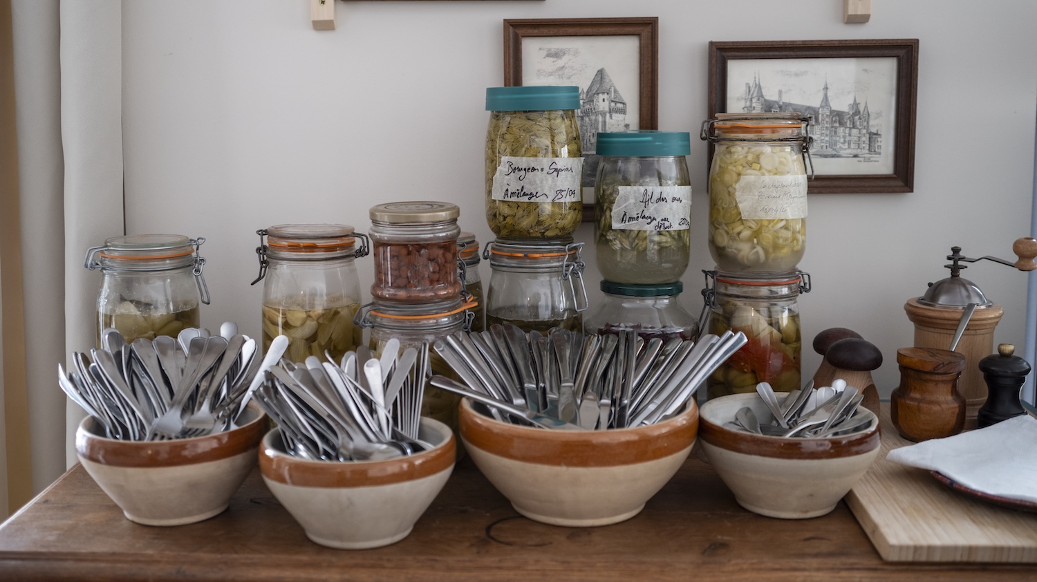Bols de couverts en métal devant des bocaux de conserves sur un buffet en bois.