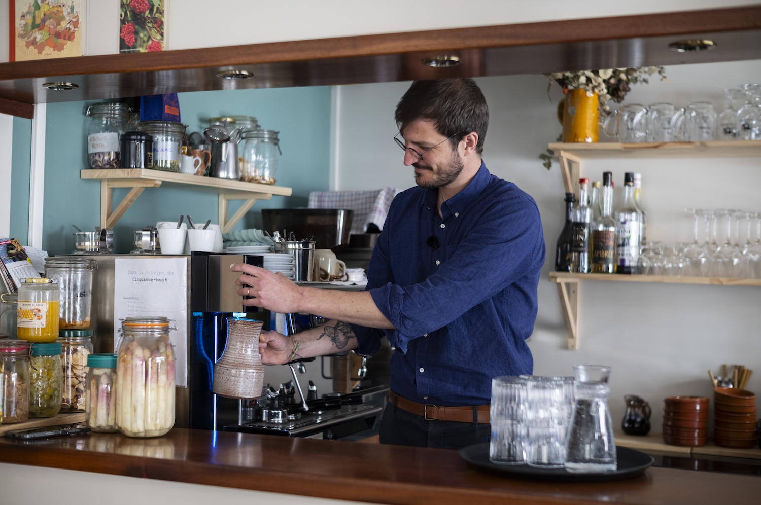 Homme préparant une boisson chaude derrière le comptoir d’un café bien décoré.