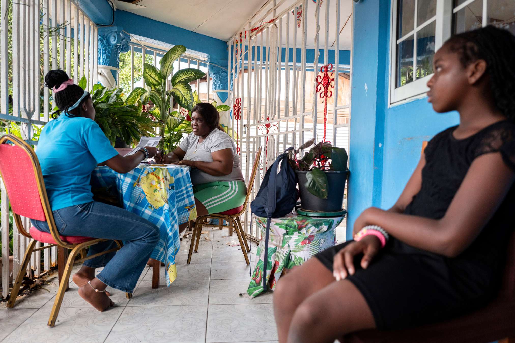 Trois femmes discutent à une table pendant qu'une jeune fille les observe depuis une chaise.