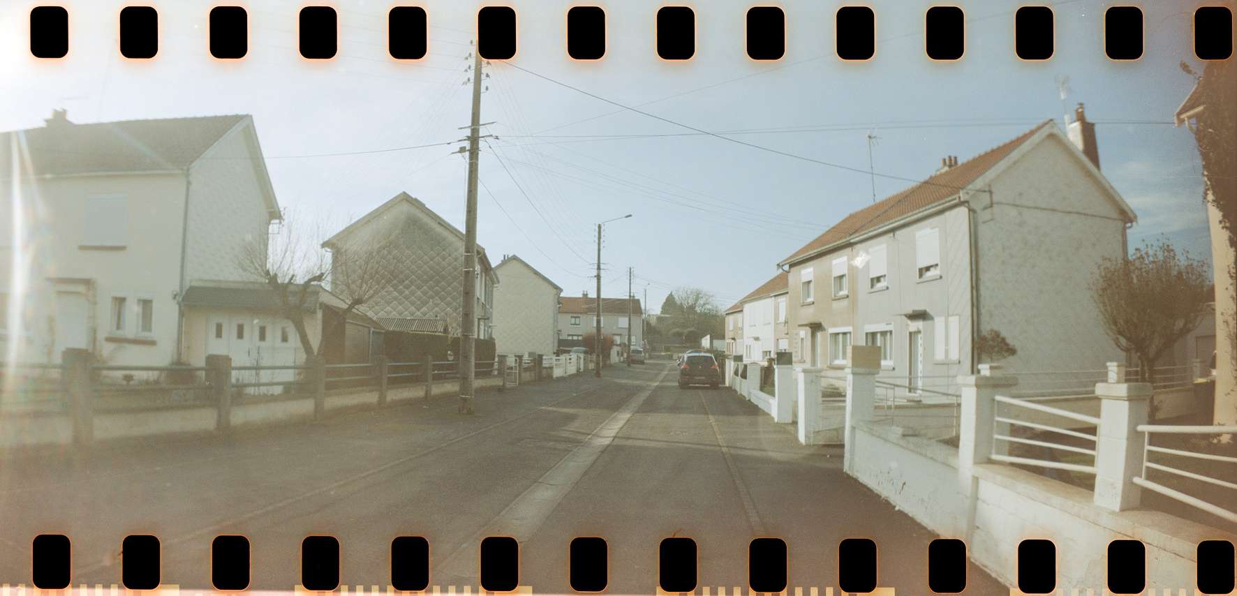 Rue résidentielle calme avec maisons alignées, ciel dégagé et poteaux électriques visibles.