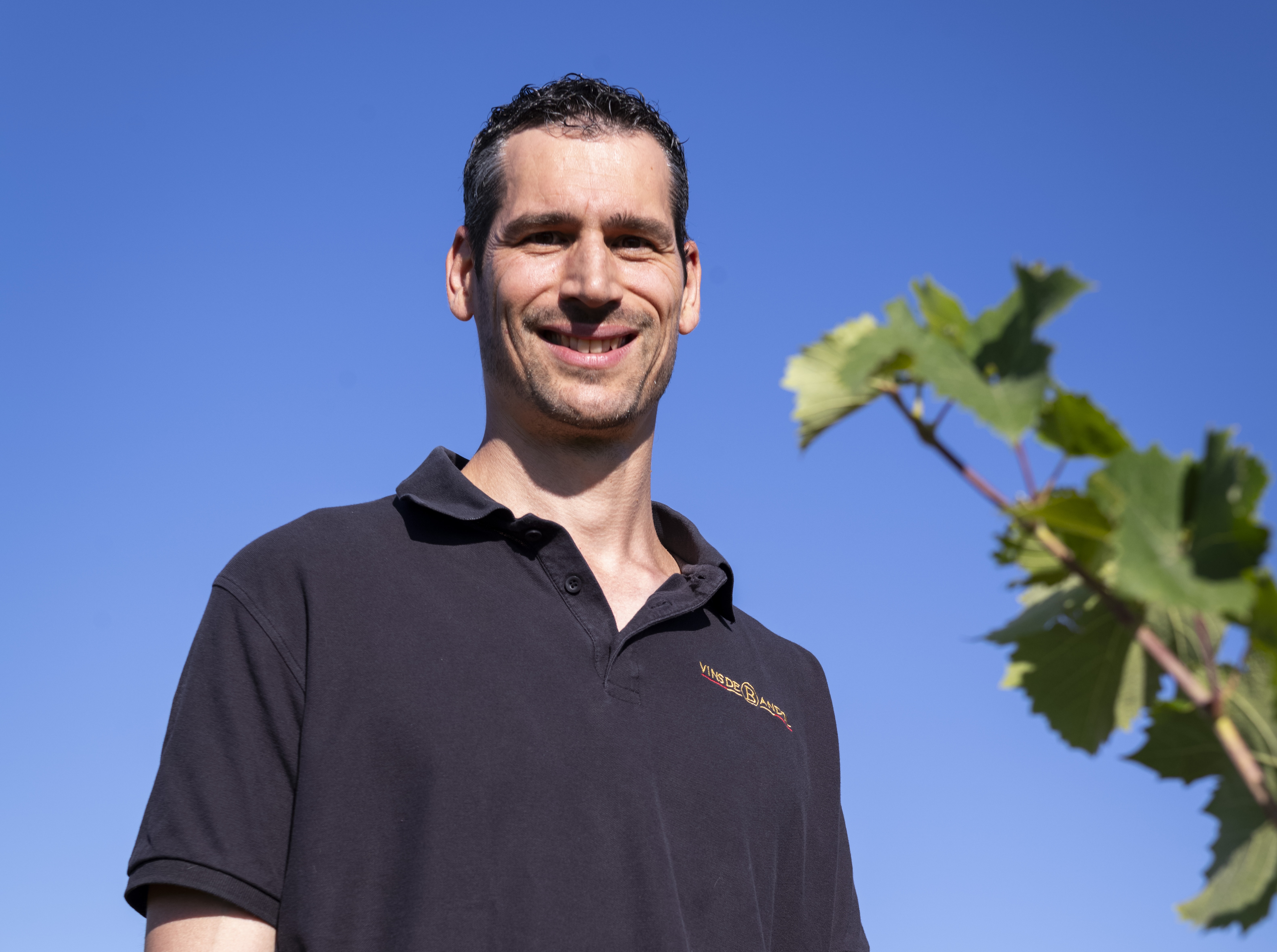 Homme souriant debout à l'extérieur près d'une vigne sous un ciel bleu clair