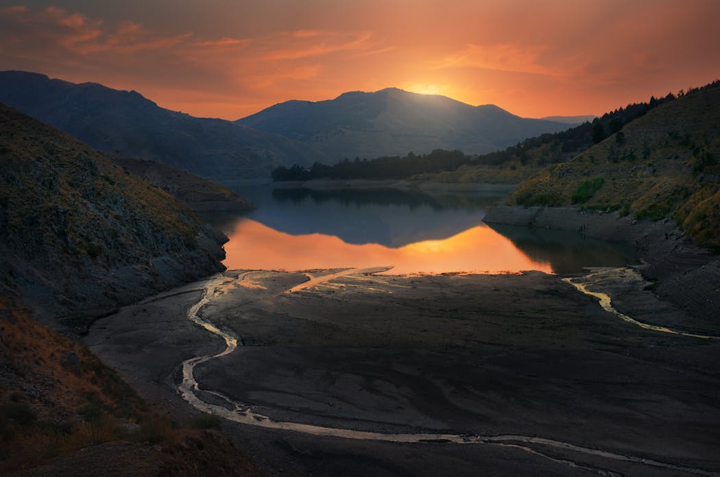 Coucher de soleil sur un lac asséché entouré de montagnes et vallées boisées