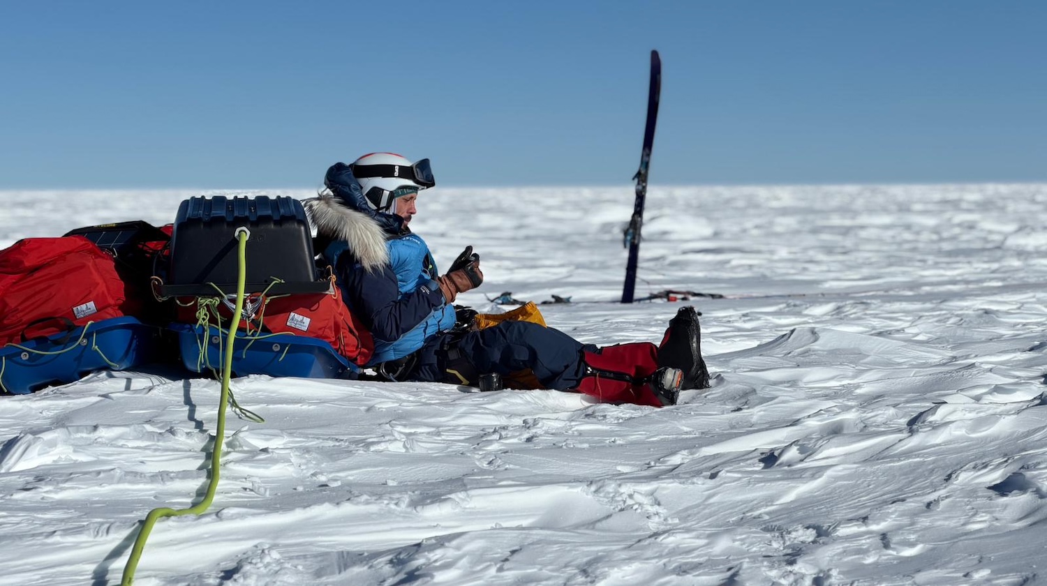 Explorateur assis sur la neige avec équipement, mangeant sous un ciel bleu dégagé en Antarctique