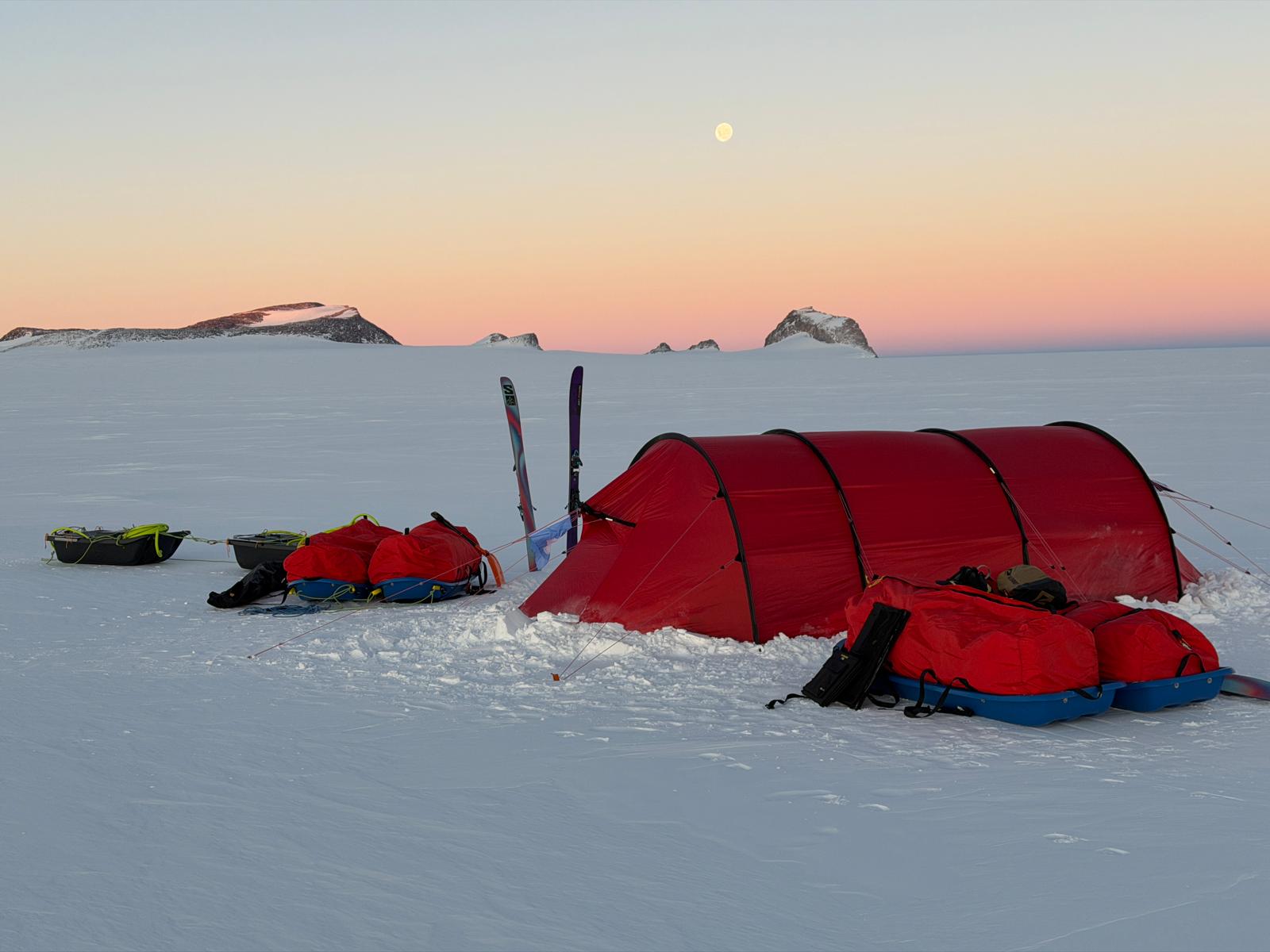 Tente rouge et équipements sur la neige au coucher du soleil en milieu polaire