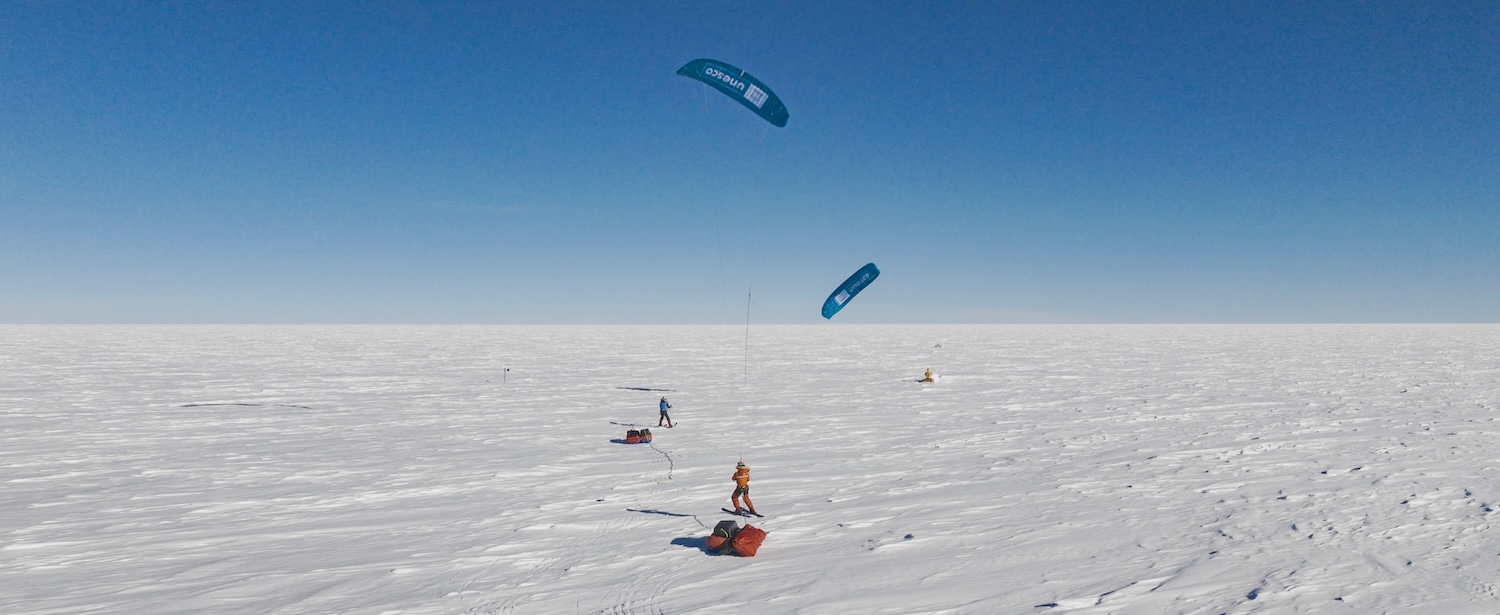Explorateurs tirés par des cerfs-volants sur une vaste étendue glacée sous un ciel bleu