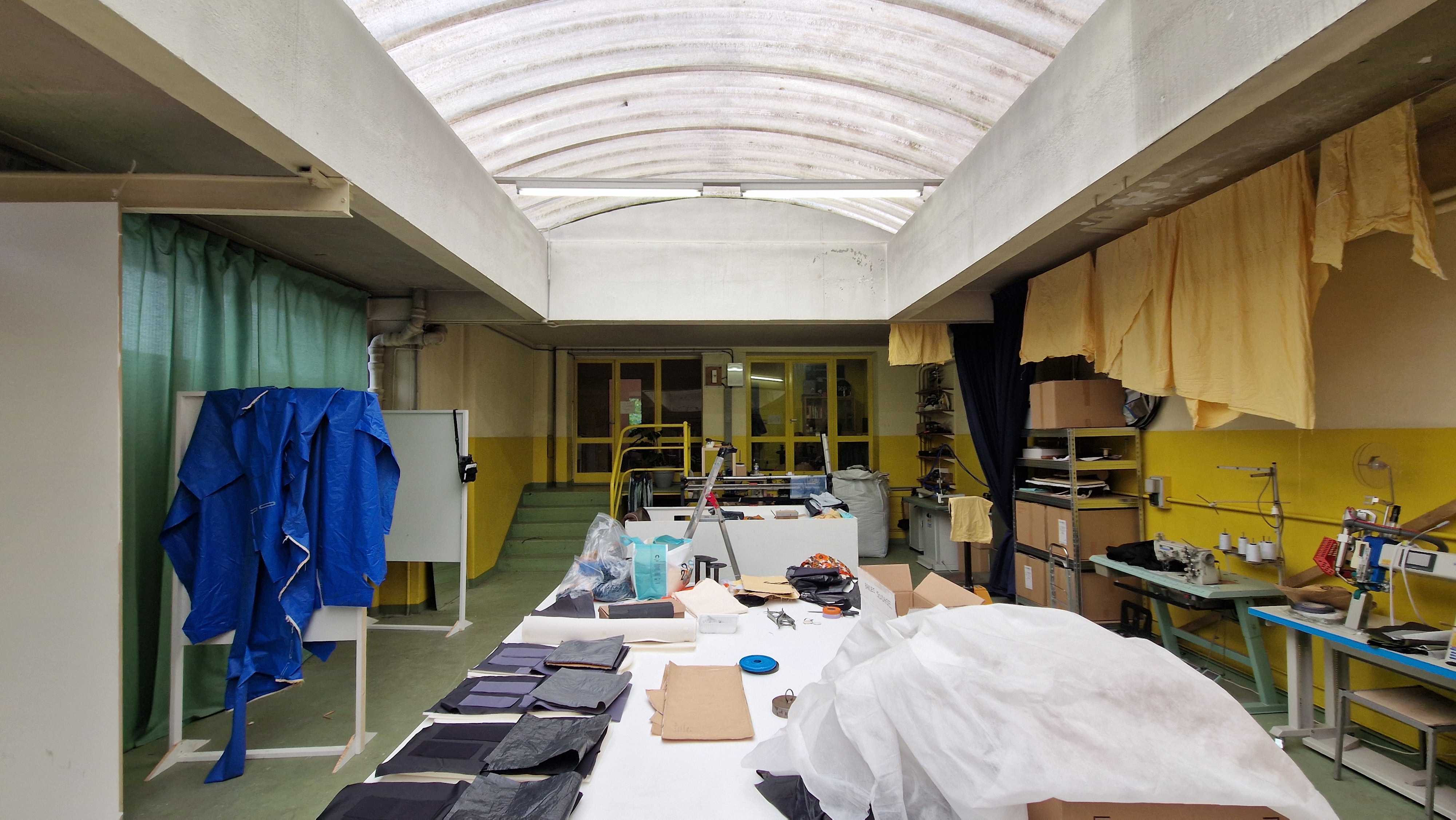Atelier de couture lumineux avec tables de travail, tissus, machines à coudre et étagères de rangement