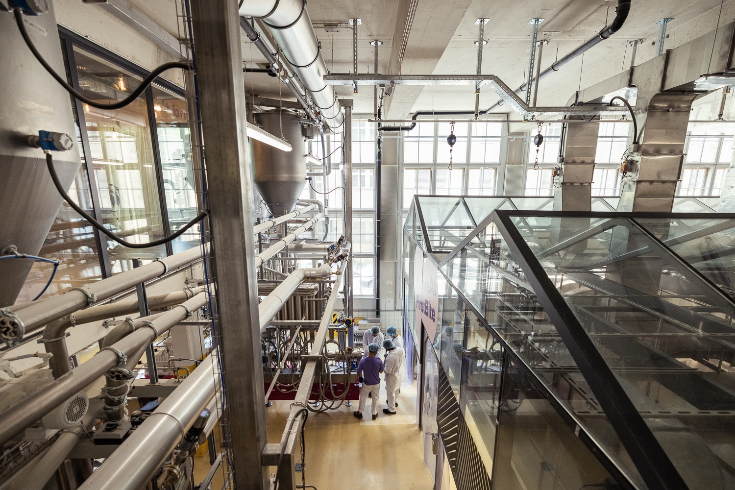 Deux personnes travaillent dans une usine moderne avec de grandes machines industrielles et des tuyaux.