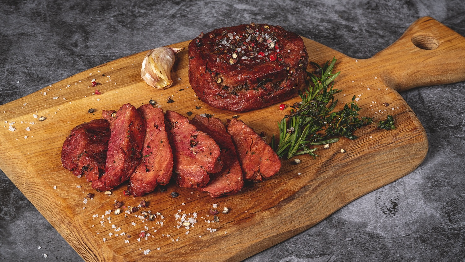 Tranches de steak végétal sur planche en bois avec herbes, ail rôti et sel.