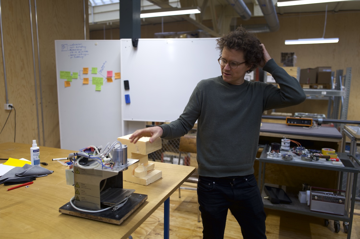 Un homme examine un appareil électronique dans un atelier avec tableau blanc et notes.