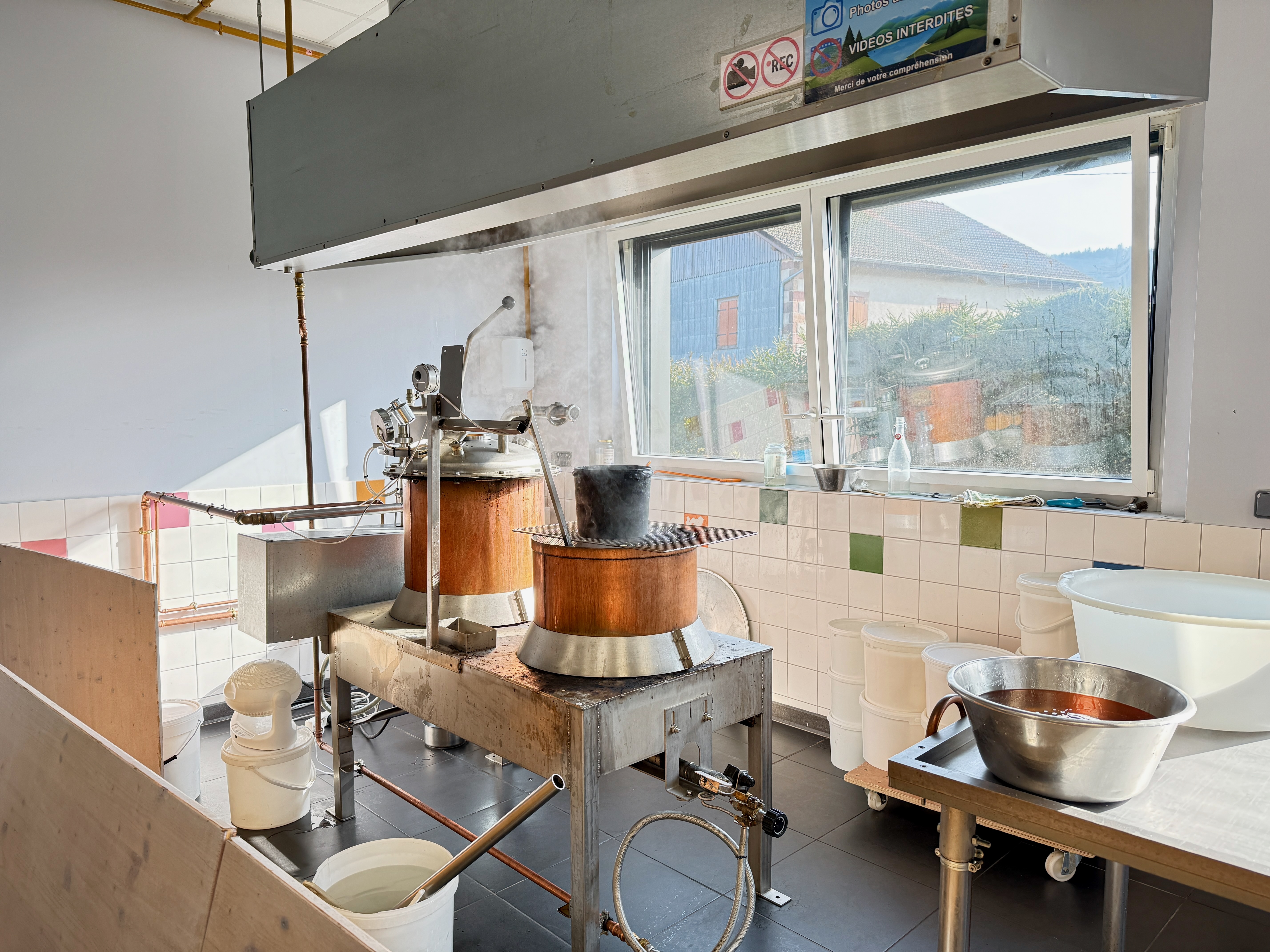 Atelier de fabrication avec cuve en cuivre et équipement industriel près d'une fenêtre.