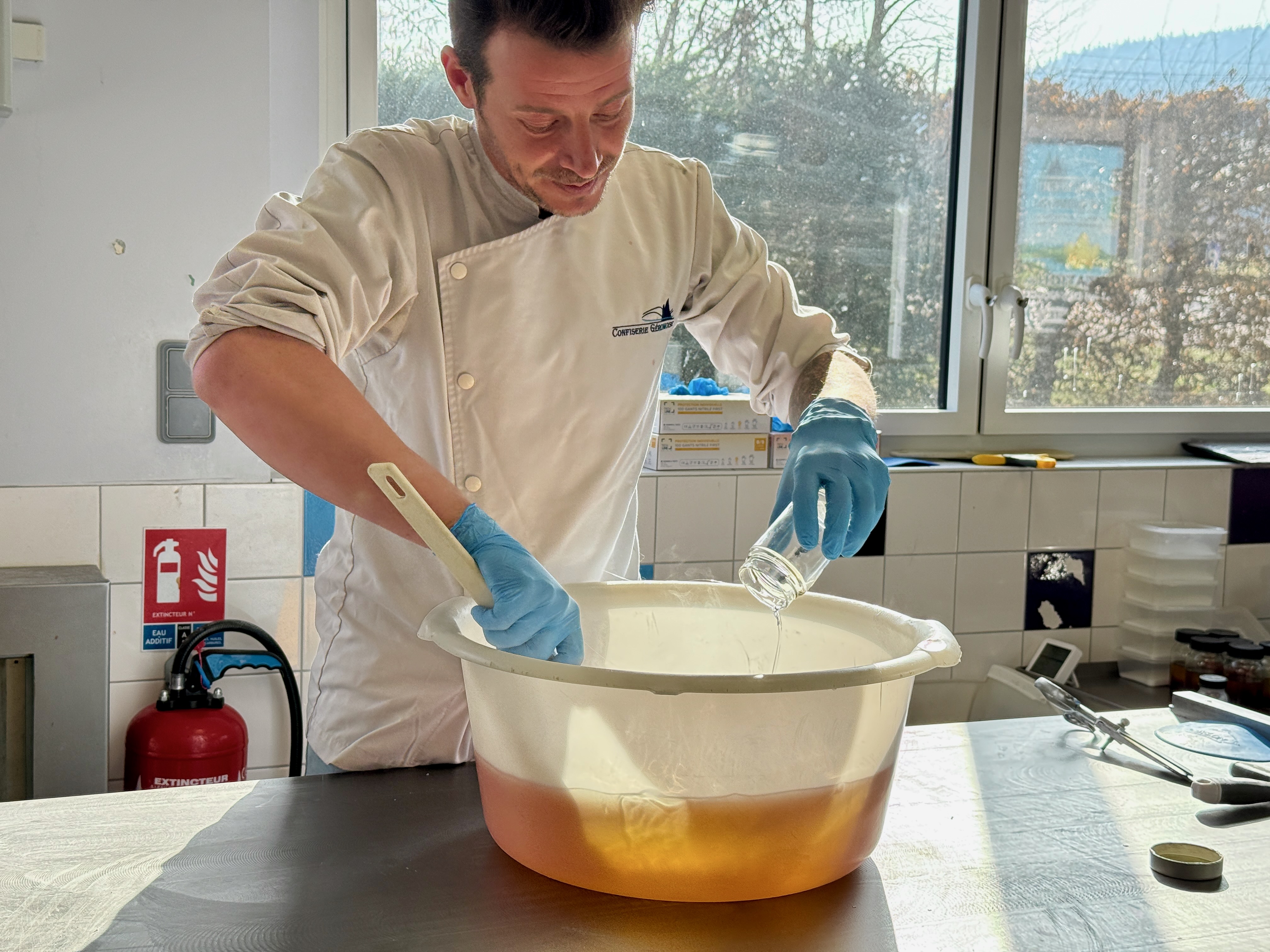 Un homme en blouse prépare un mélange dans un grand récipient blanc.