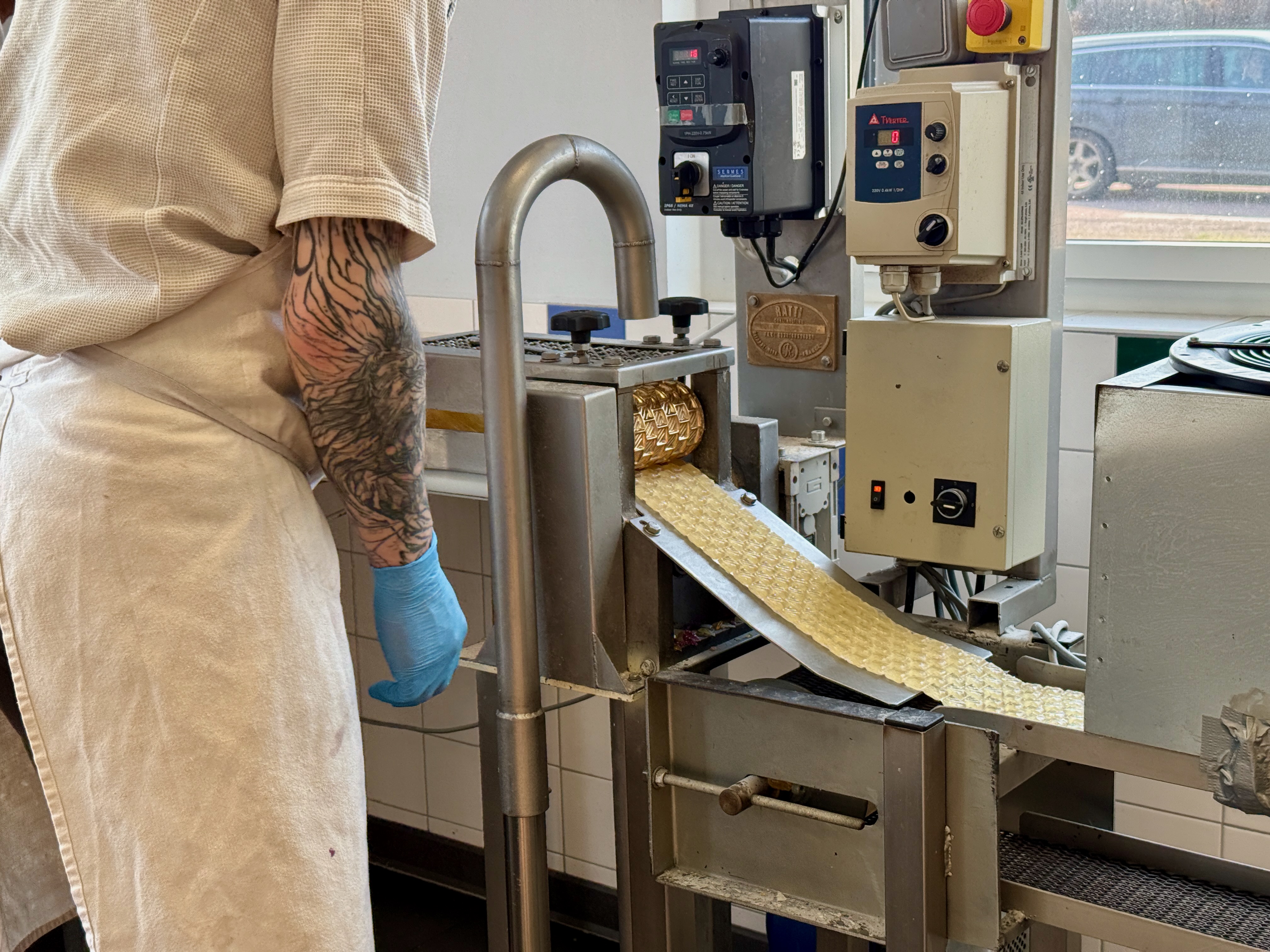 Personne tatouée en blouse fabrique des bonbons avec une machine industrielle.