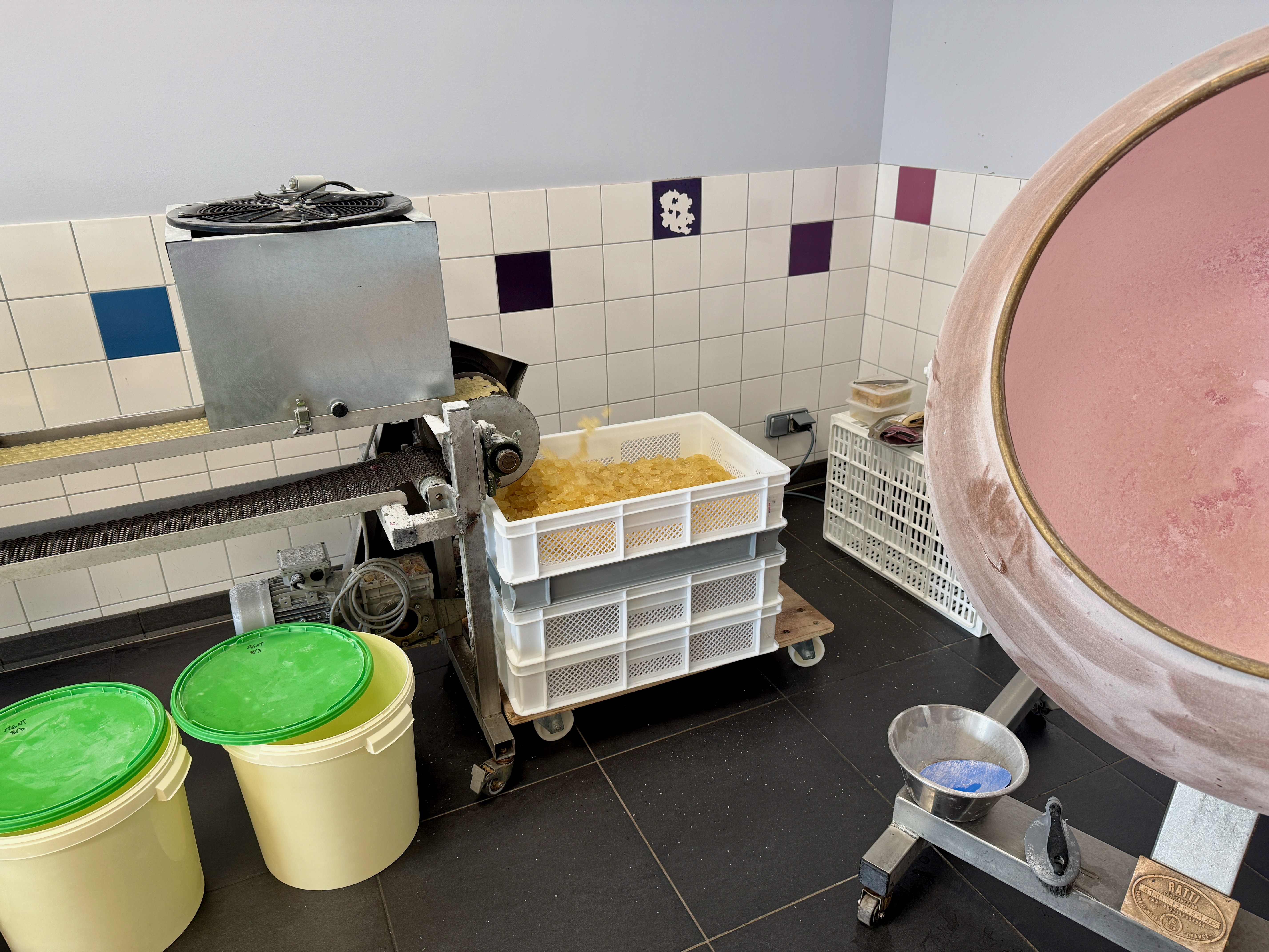 Salle de production avec machine, bacs de pâtes et conteneurs colorés.