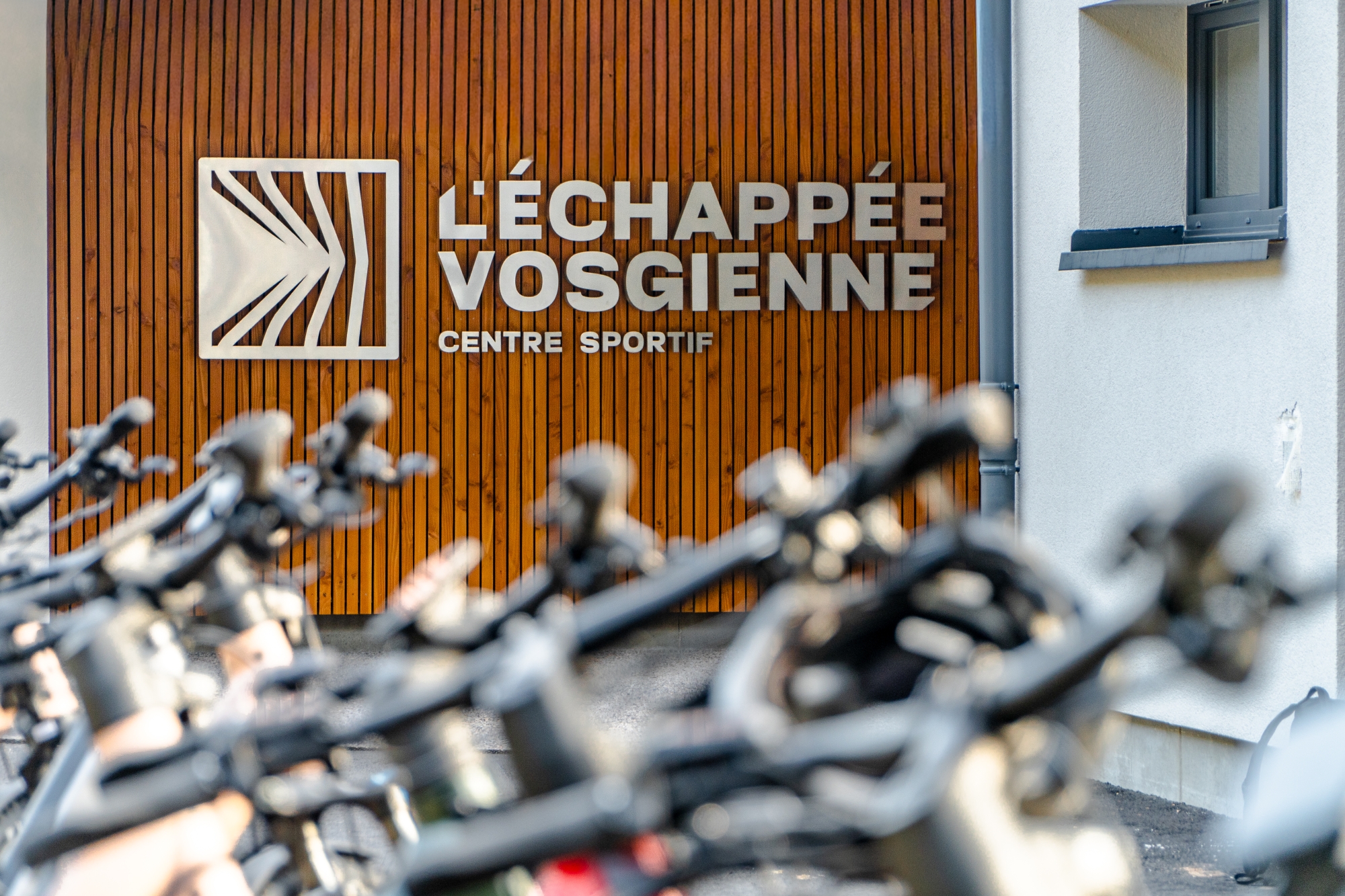 Façade en bois du centre sportif L'Échappée Vosgienne avec rangée de vélos au premier plan.
