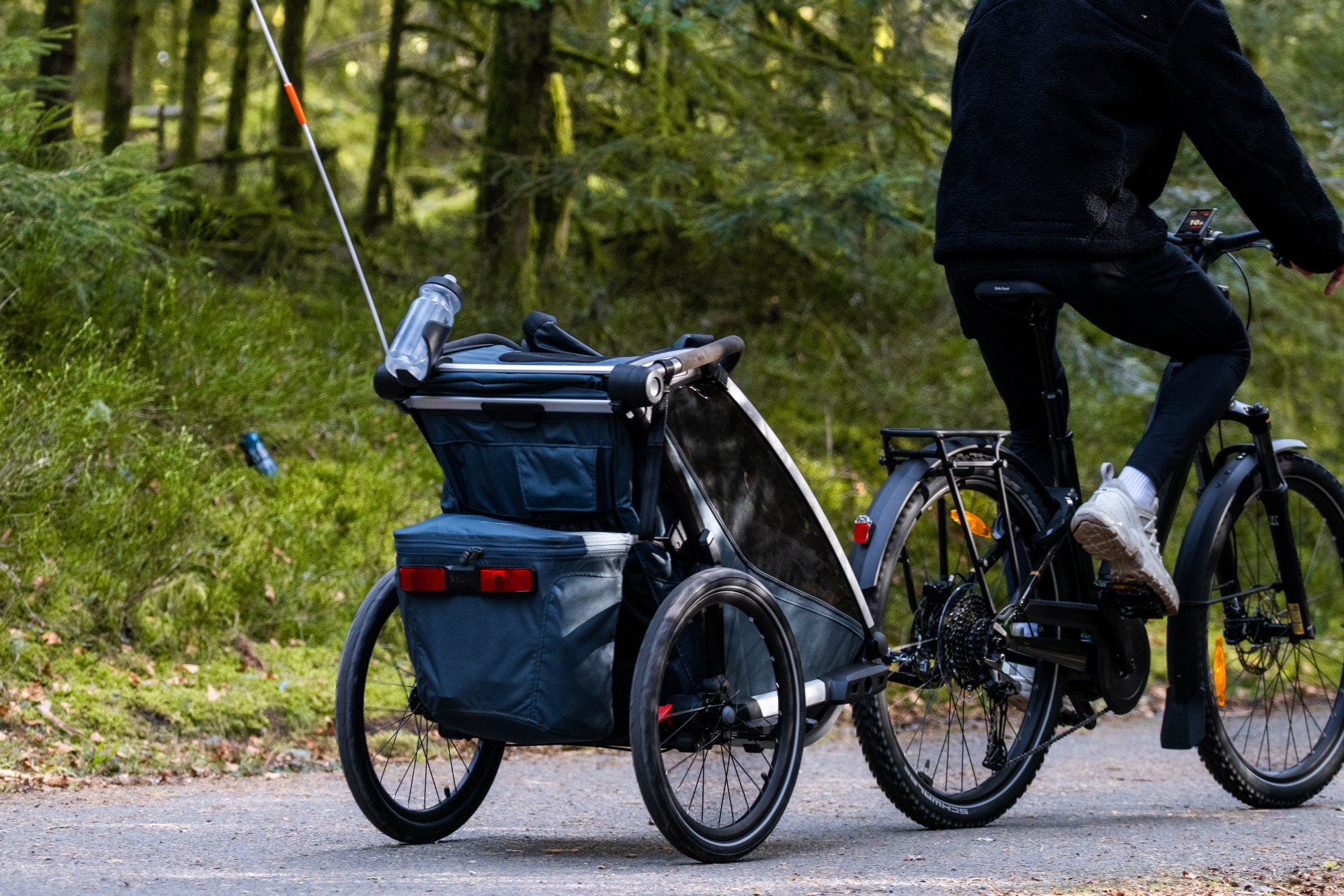 Cycliste tirant une remorque à vélo dans un chemin forestier.