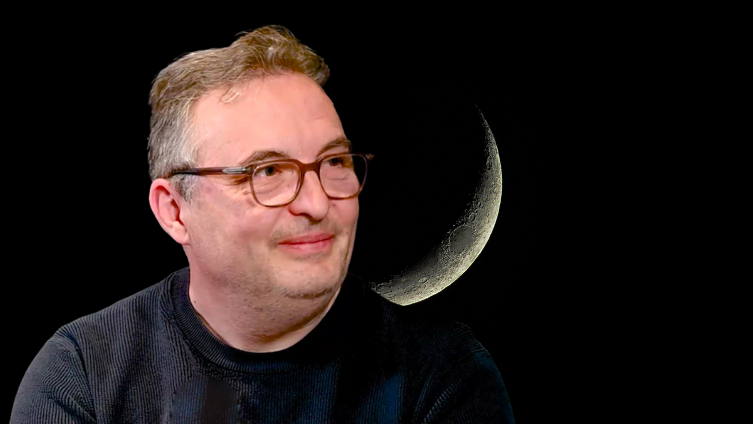 Un homme souriant avec des lunettes devant une lune en croissant.