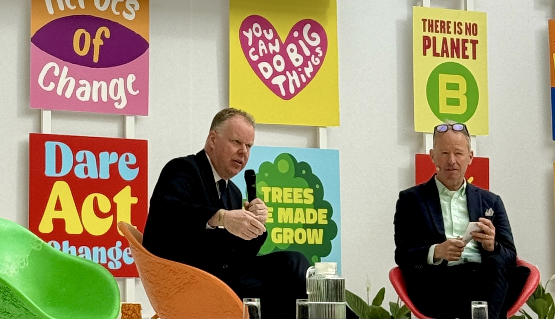 Deux hommes discutent devant des affiches colorées sur l'environnement et le changement climatique.