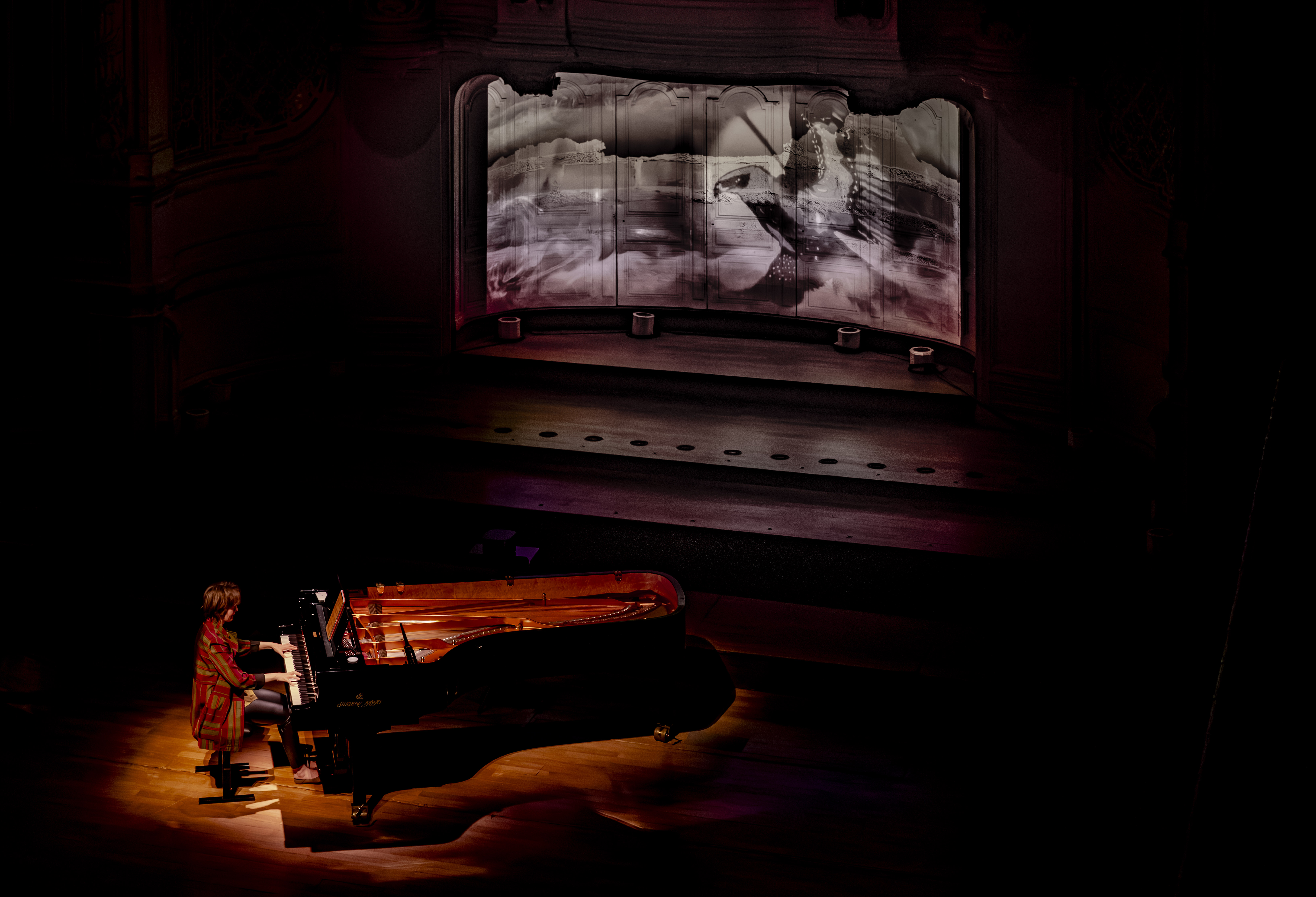 Pianiste jouant sur scène avec une projection artistique en arrière-plan, ambiance sombre et dramatique.