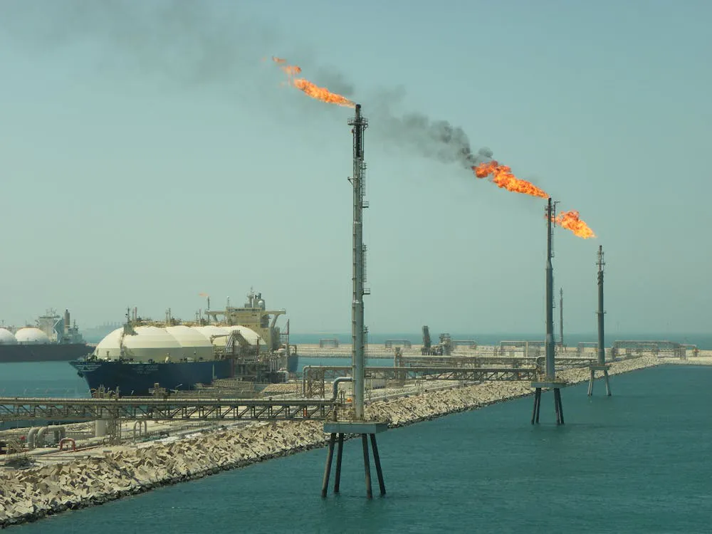 Torches de gaz brûlant sur un site industriel maritime avec réservoirs en arrière-plan.