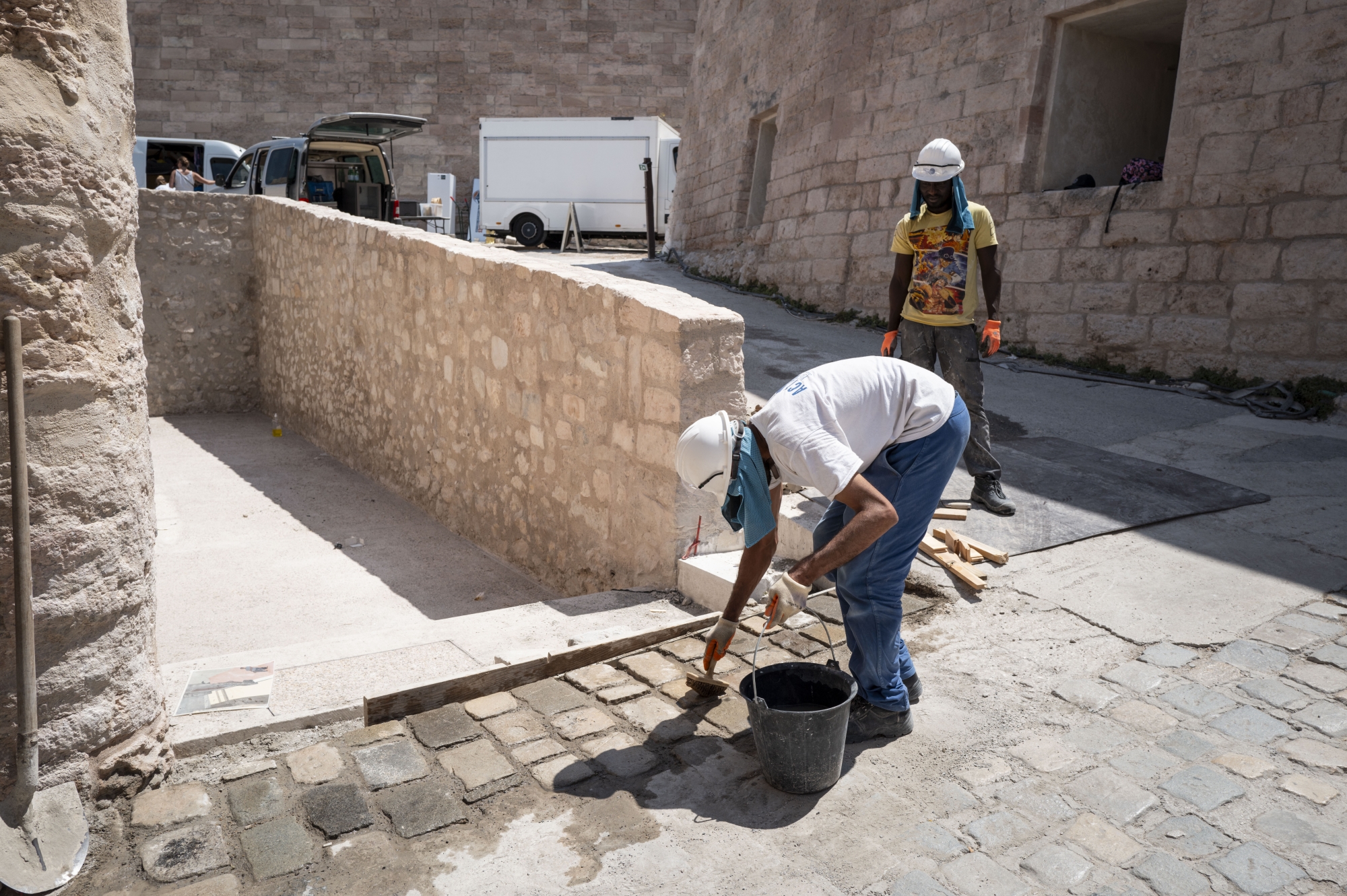 Travailleurs en casques effectuant des travaux de pavage dans une rue ensoleillée.