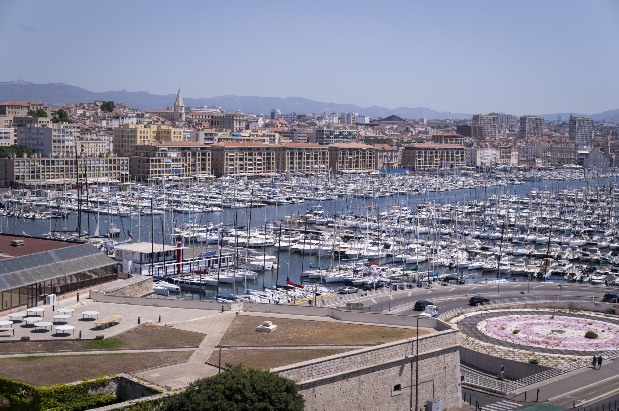 Vue du port de Marseille avec de nombreux bateaux et des bâtiments en arrière-plan.