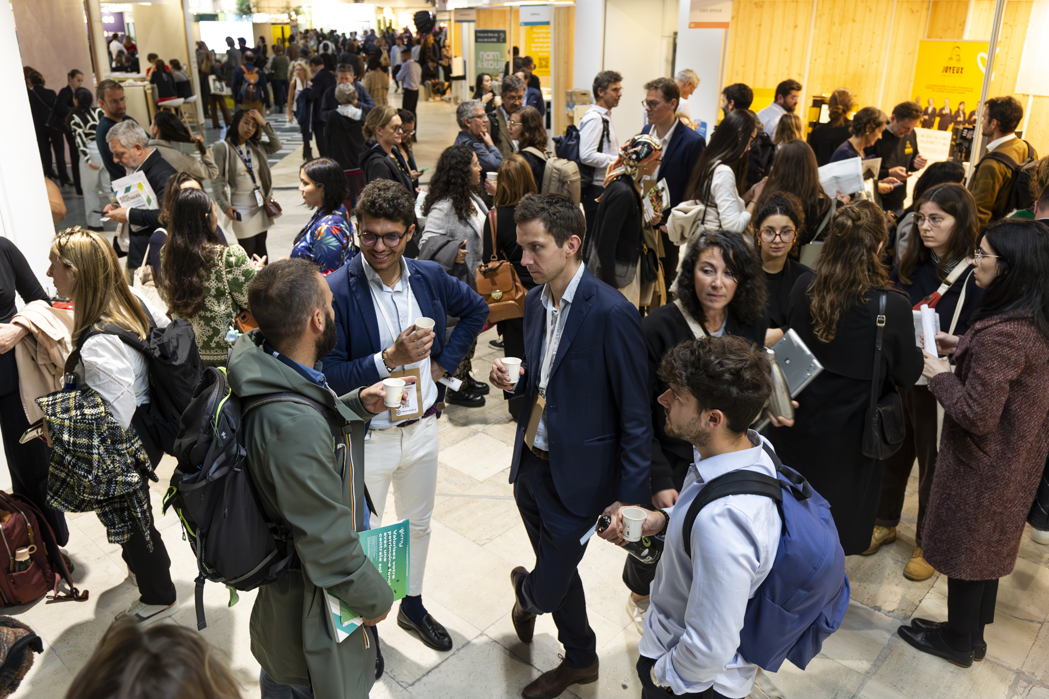 Des personnes discutent lors d'un événement professionnel, avec des stands et des brochures.