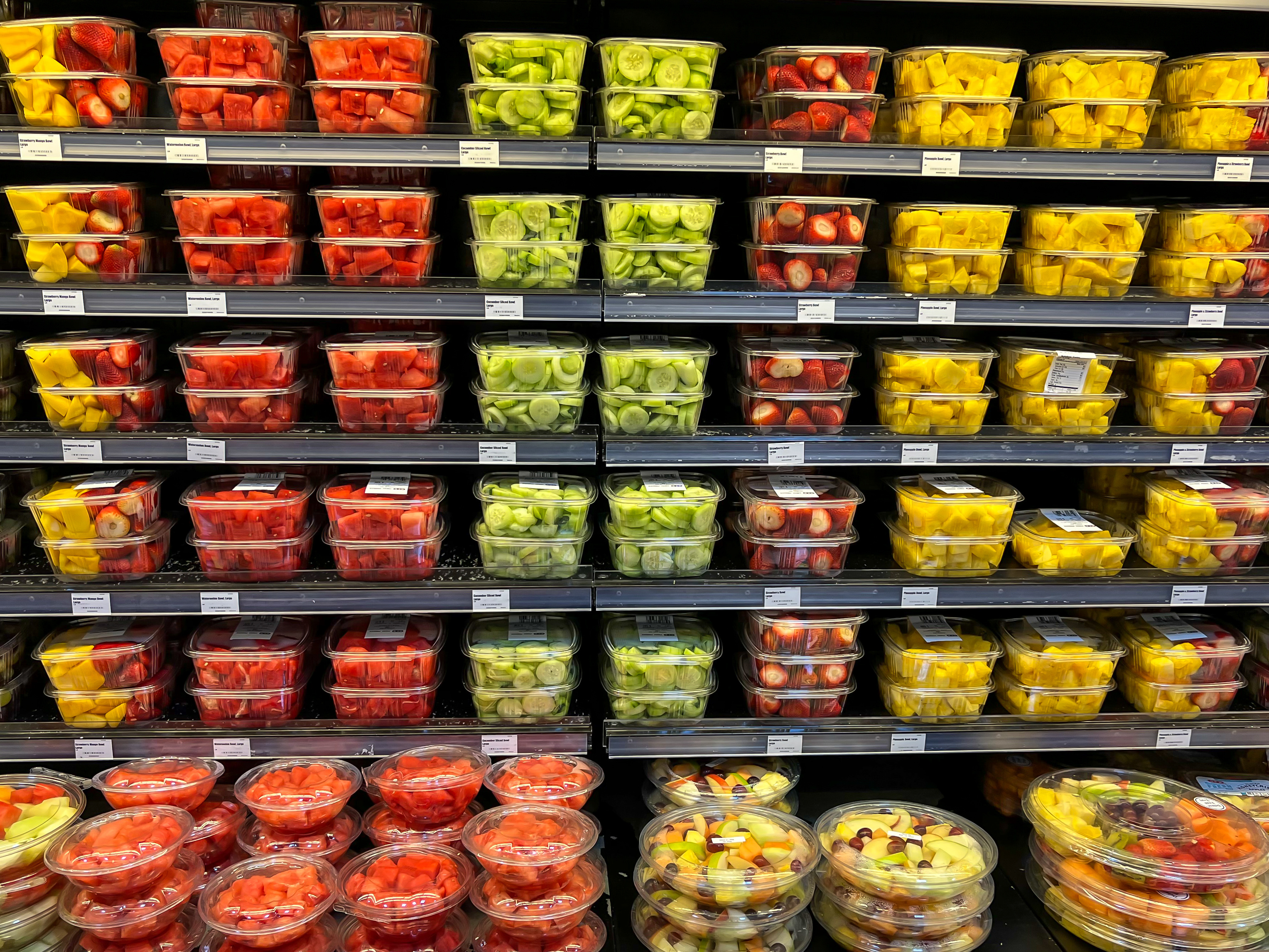 Rayons de supermarché avec des barquettes de fruits coupés colorés empilés.