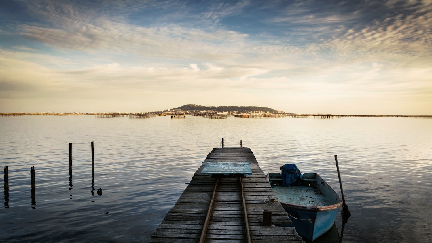 Un ponton en bois mène à un lac calme avec une barque bleue.