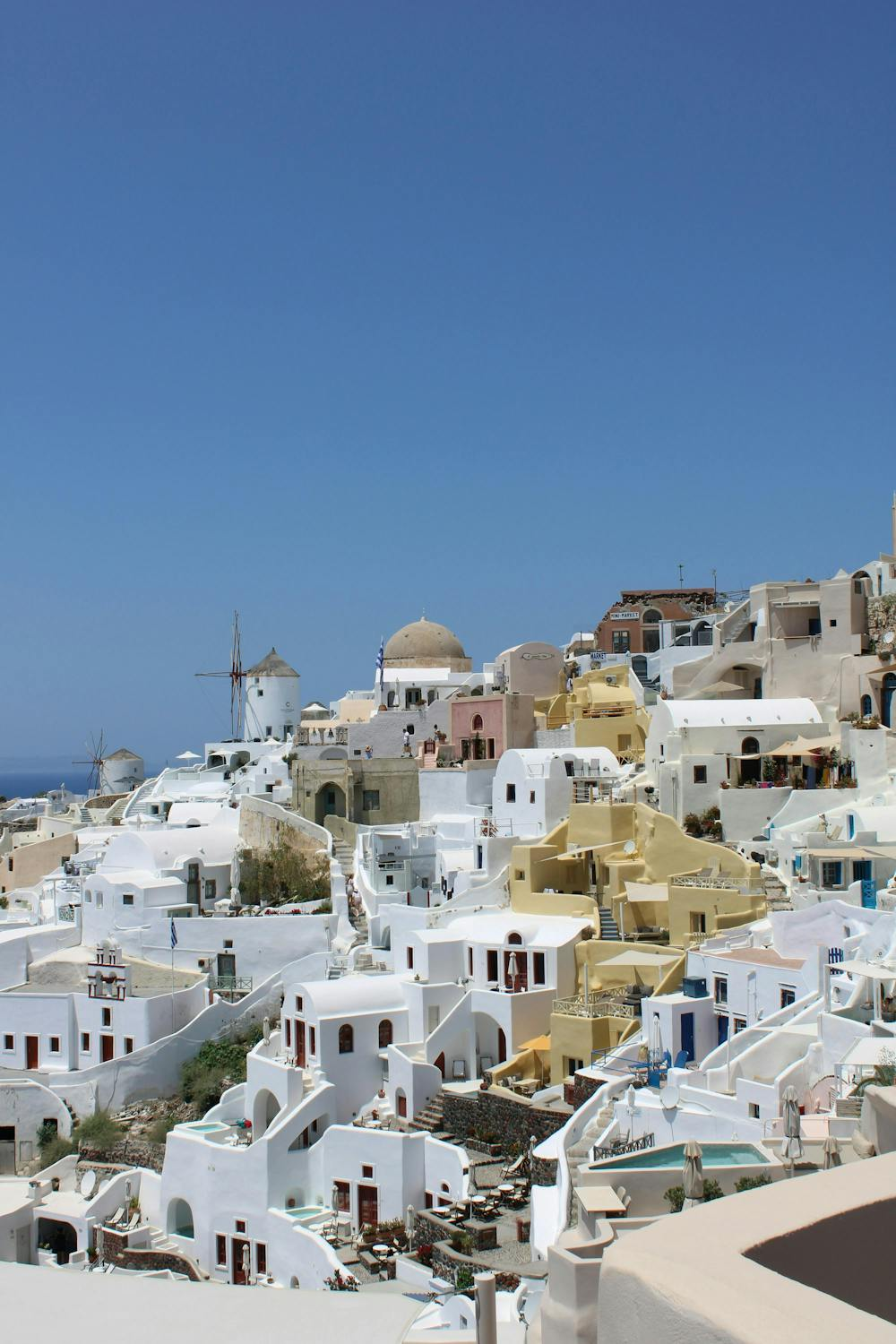 Maisons blanches et toits colorés à Santorin, avec ciel bleu et éolienne en arrière-plan.