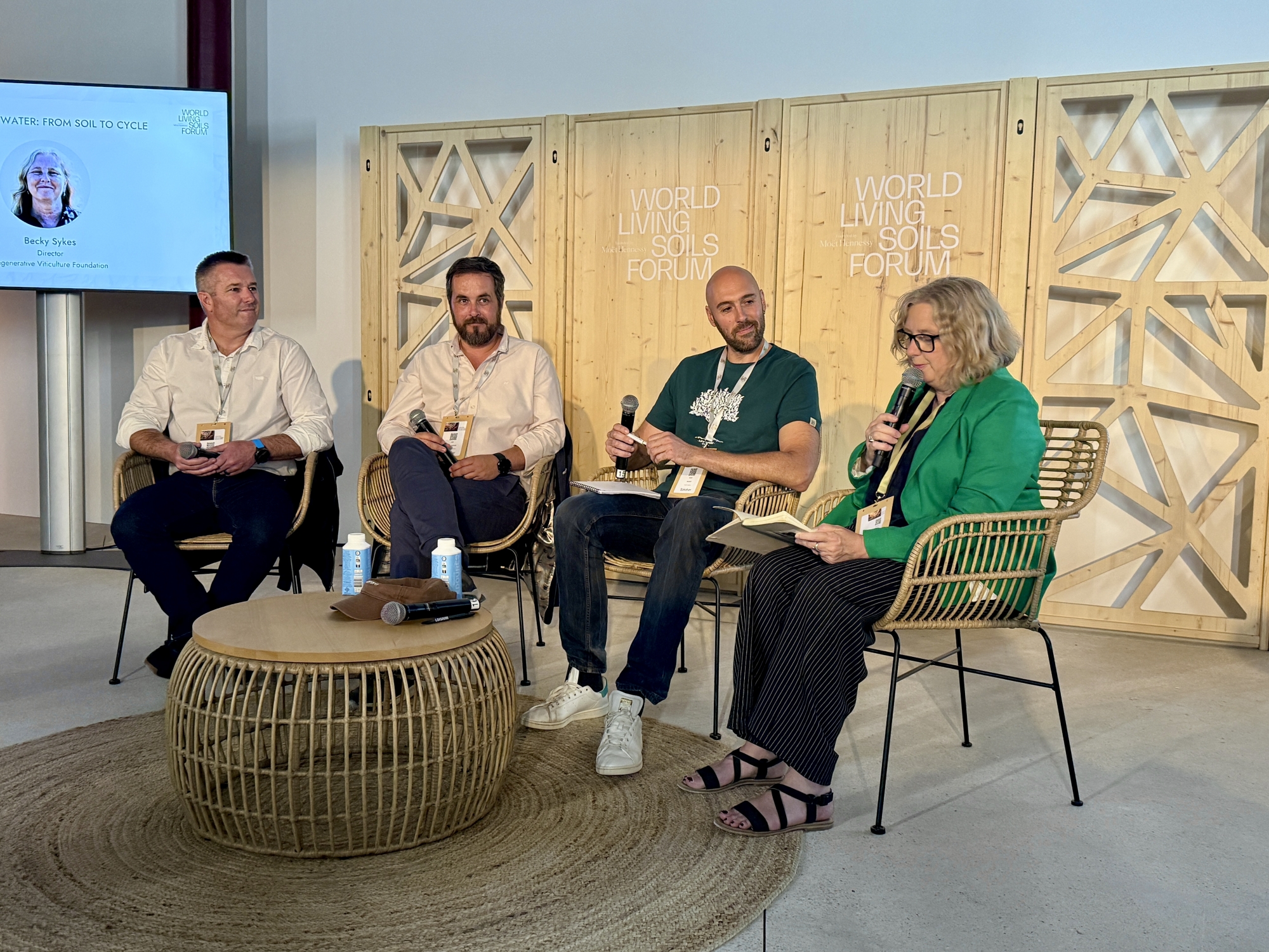 Quatre personnes discutent lors d'une conférence, assises sur une scène avec un décor en bois.