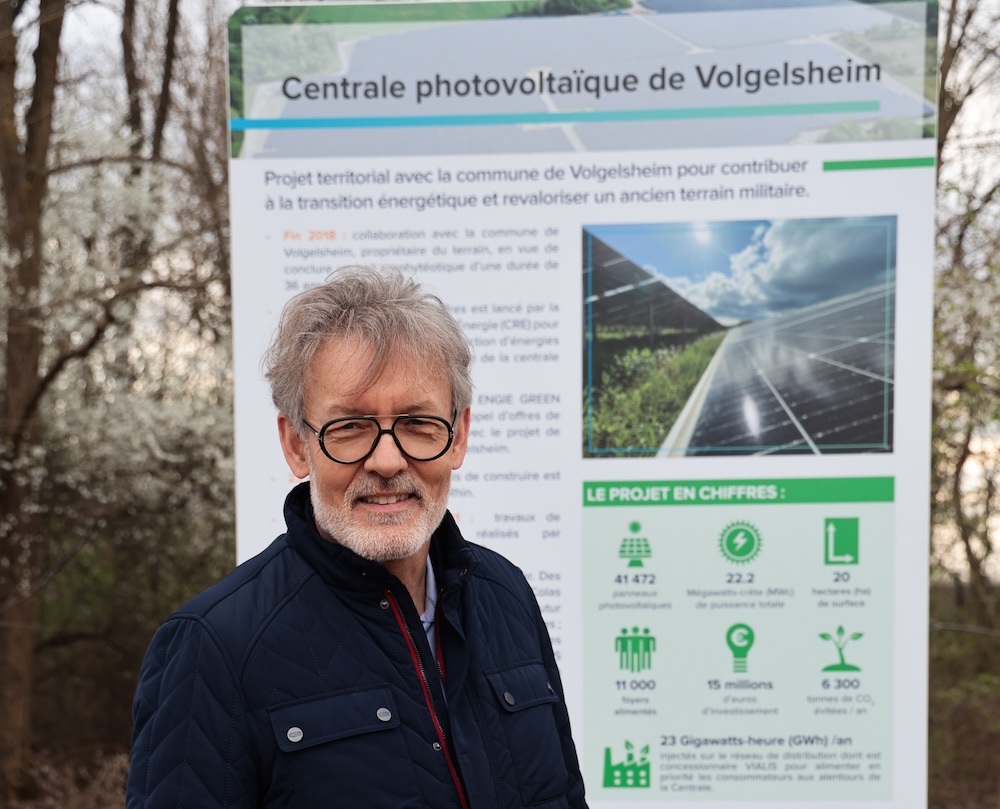 Homme souriant devant une affiche de projet de transition énergétique avec panneaux solaires.