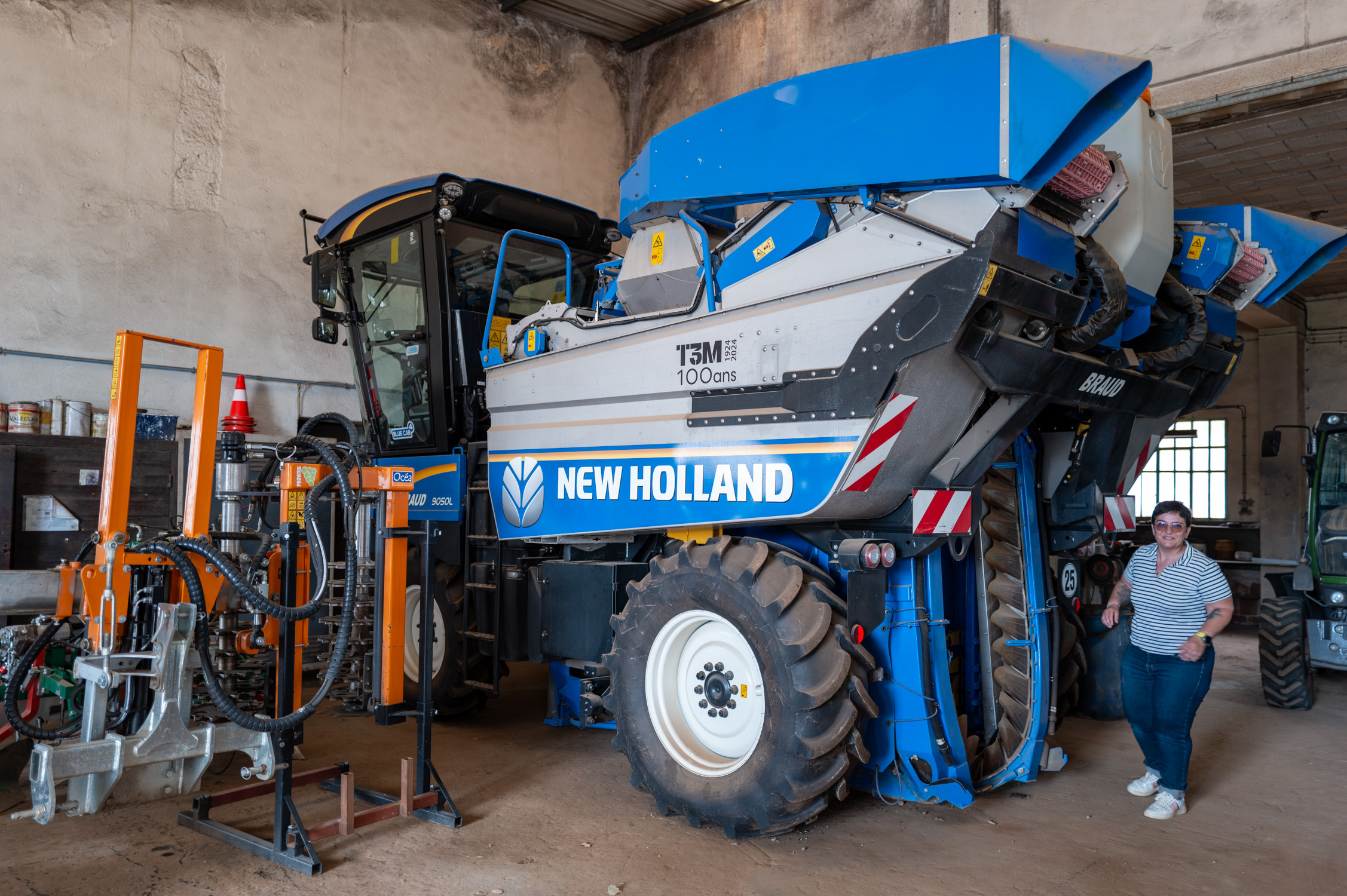 Machine agricole New Holland bleue dans un hangar avec une personne à côté.