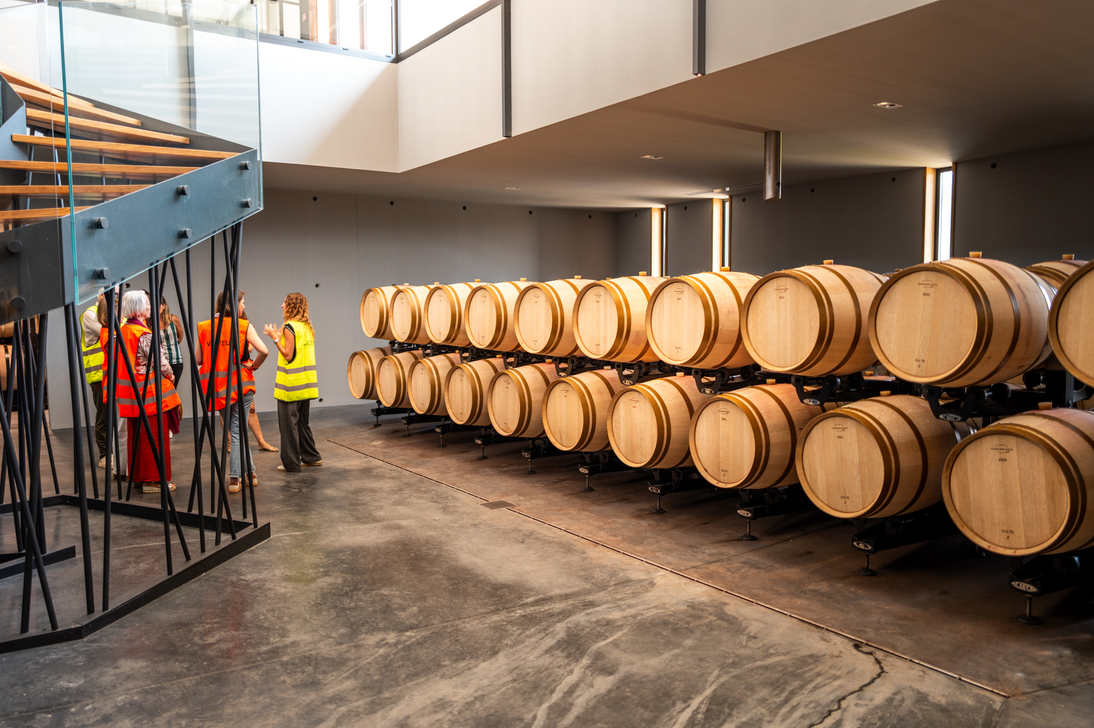Visite de cave à vin avec des barriques en bois et des visiteurs en gilets jaunes.