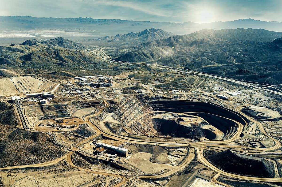 Vue aérienne d'une mine à ciel ouvert entourée de montagnes et de végétation clairsemée.
