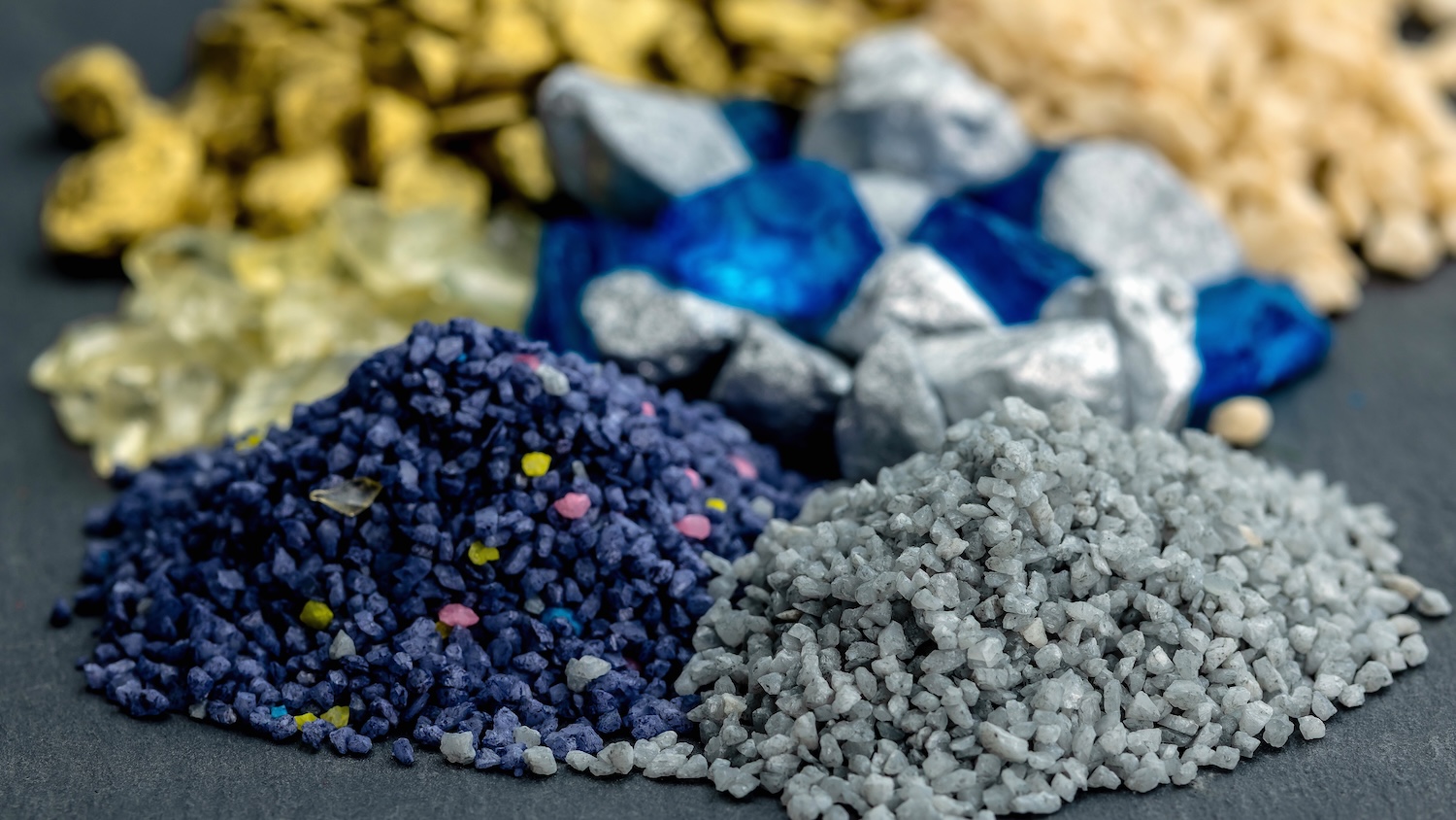 Différents tas de minerais colorés sur une surface grise.