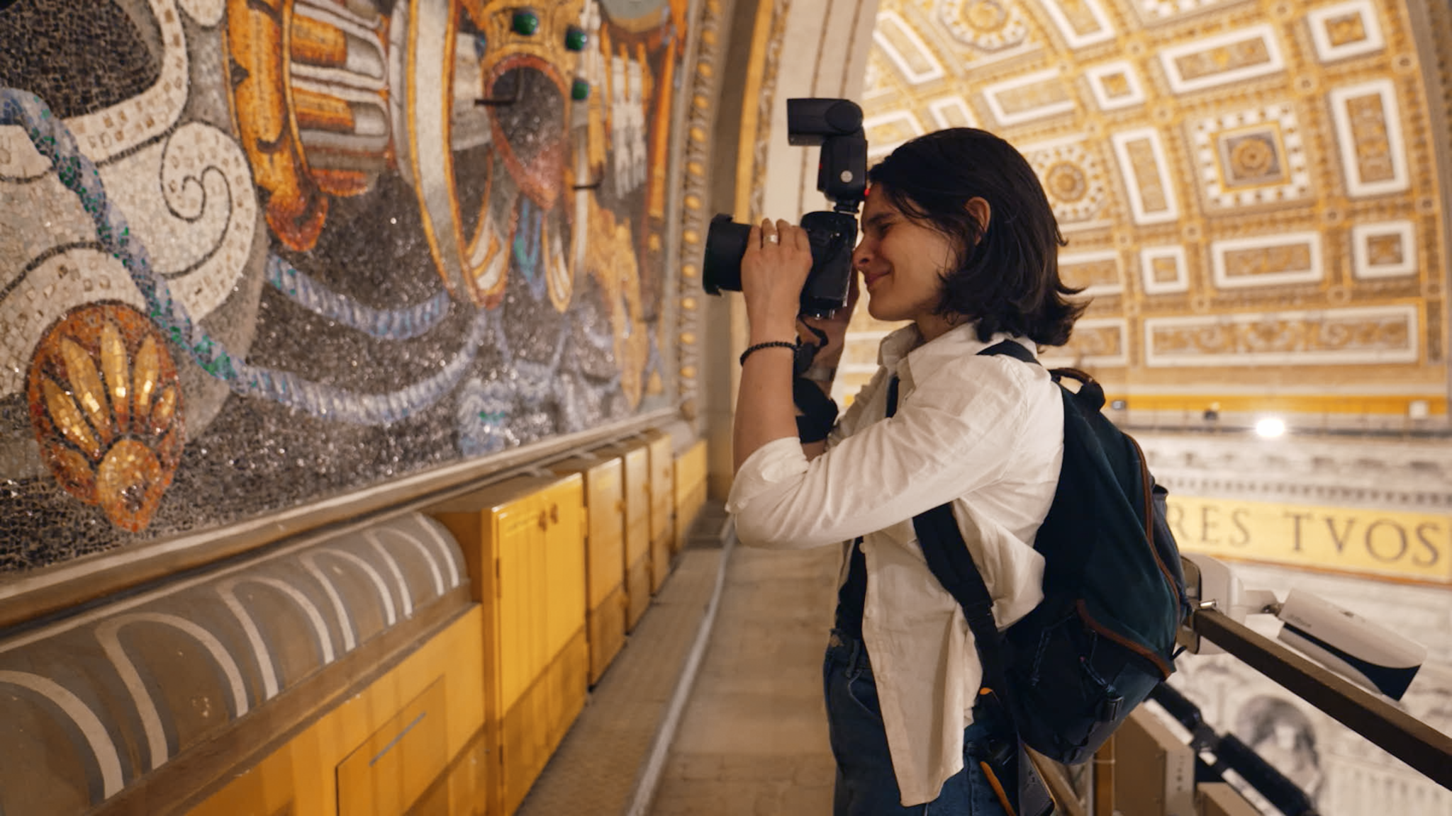 Une femme photographie une fresque dans un bâtiment richement décoré.