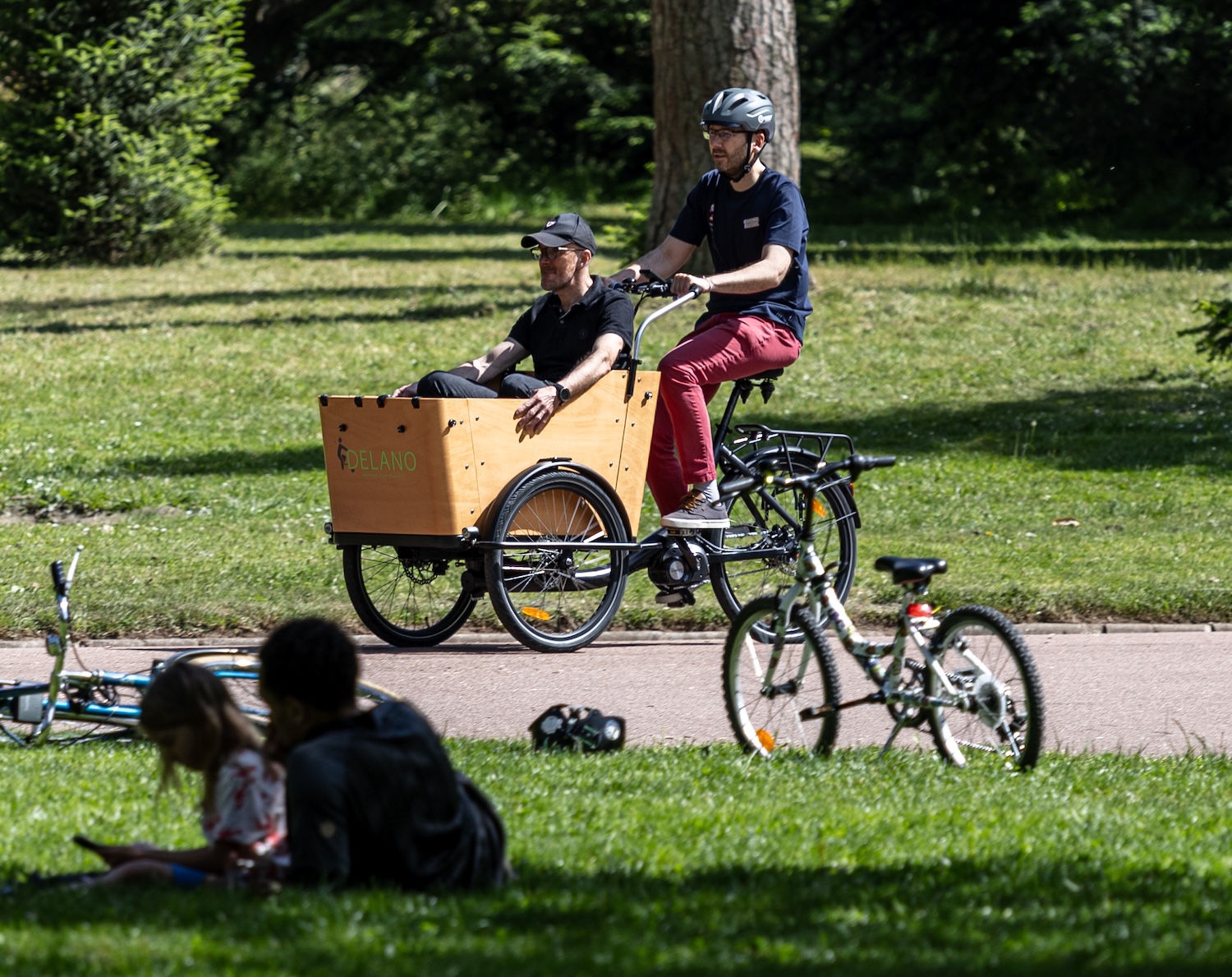 Deux personnes sur un vélo cargo dans un parc, profitant d'une journée ensoleillée.