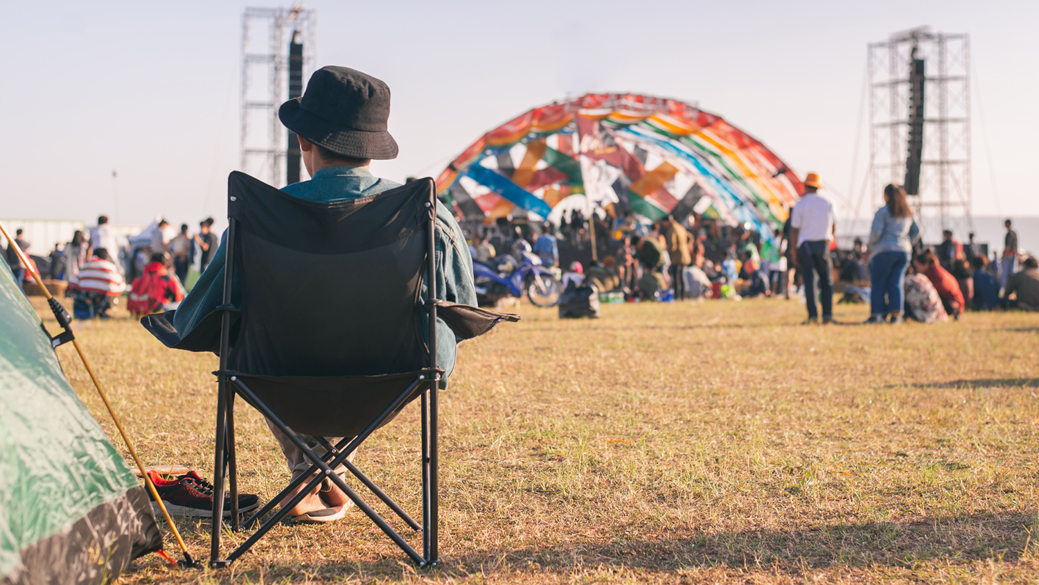 Personne assise sur une chaise regarde une scène colorée en plein air lors d'un festival.