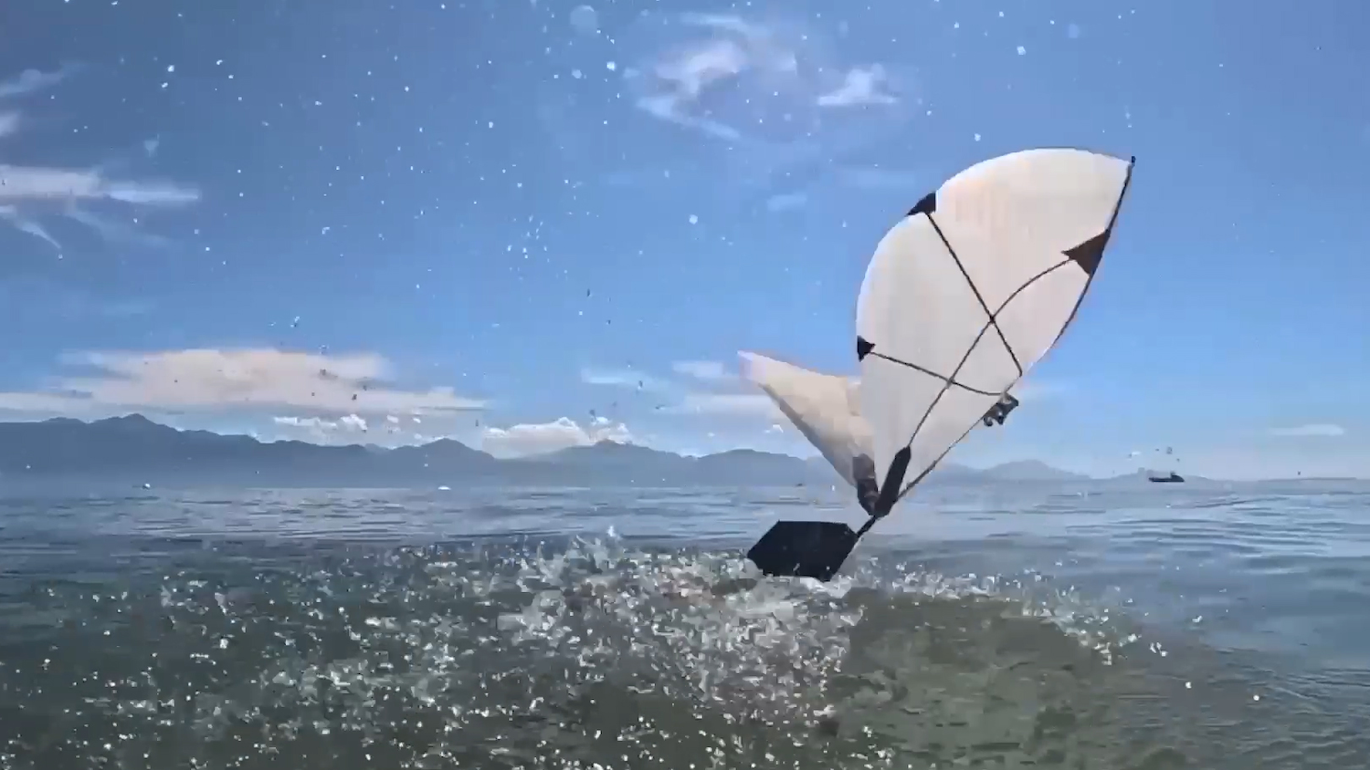 Un cerf-volant blanc survole l'océan sous un ciel bleu avec des montagnes lointaines.
