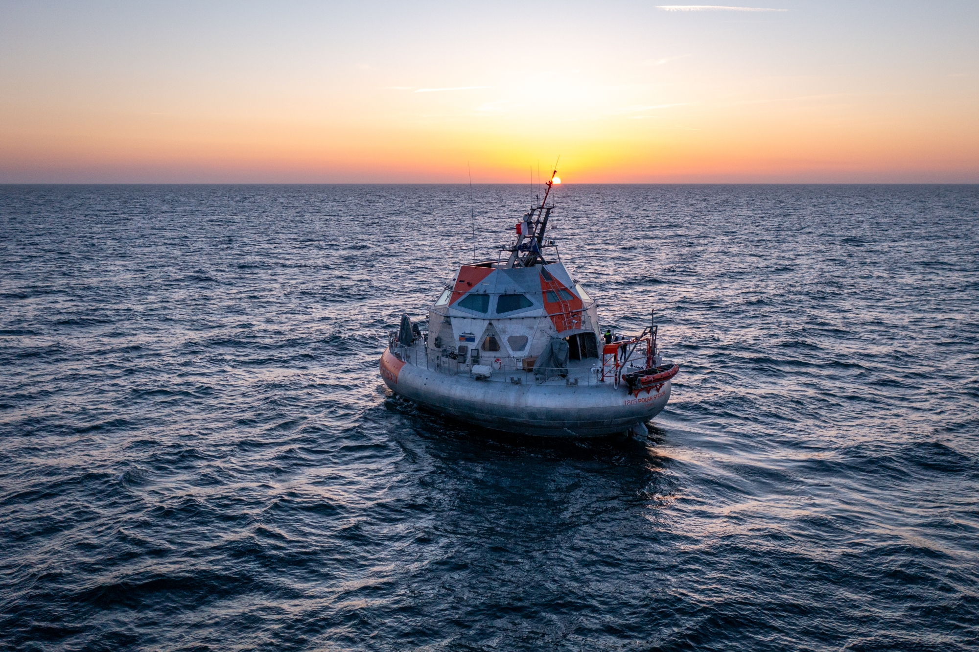 Un bateau en mer au coucher du soleil, avec un ciel coloré en arrière-plan.