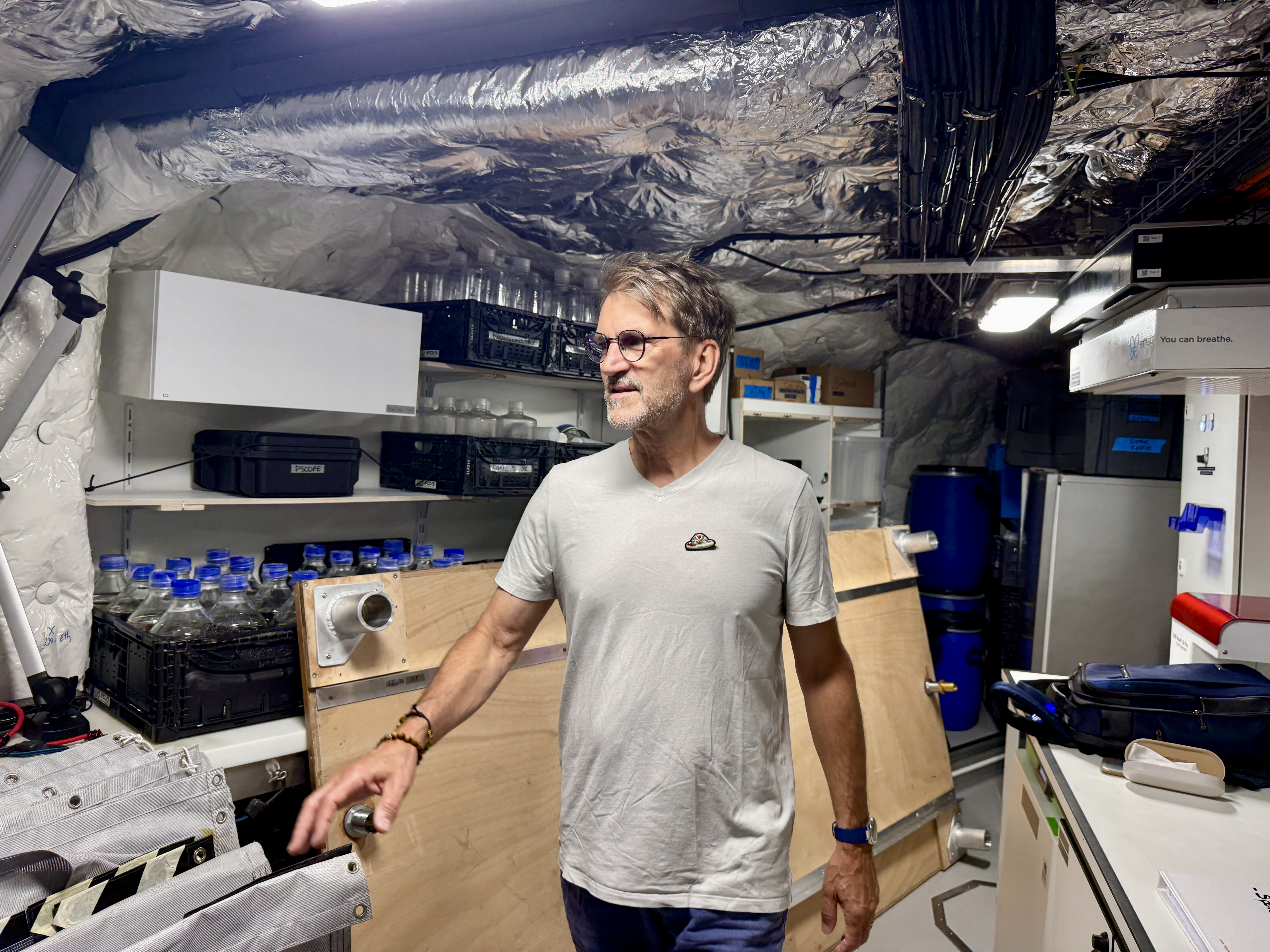 Un homme dans un sous-sol rempli d’équipements et de bouteilles en plastique.
