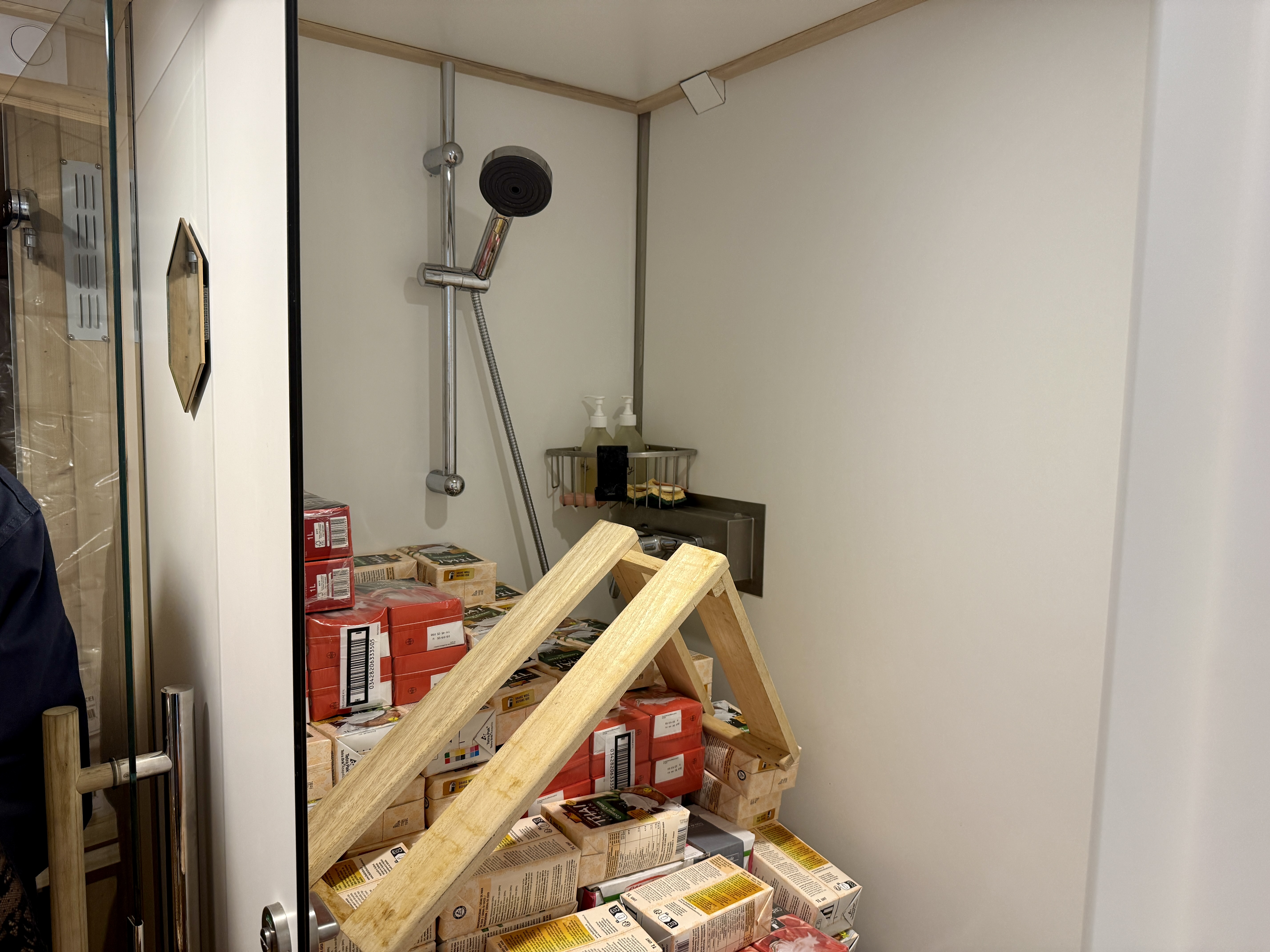 Douche transformée en espace de rangement avec des boîtes et des étagères en bois.