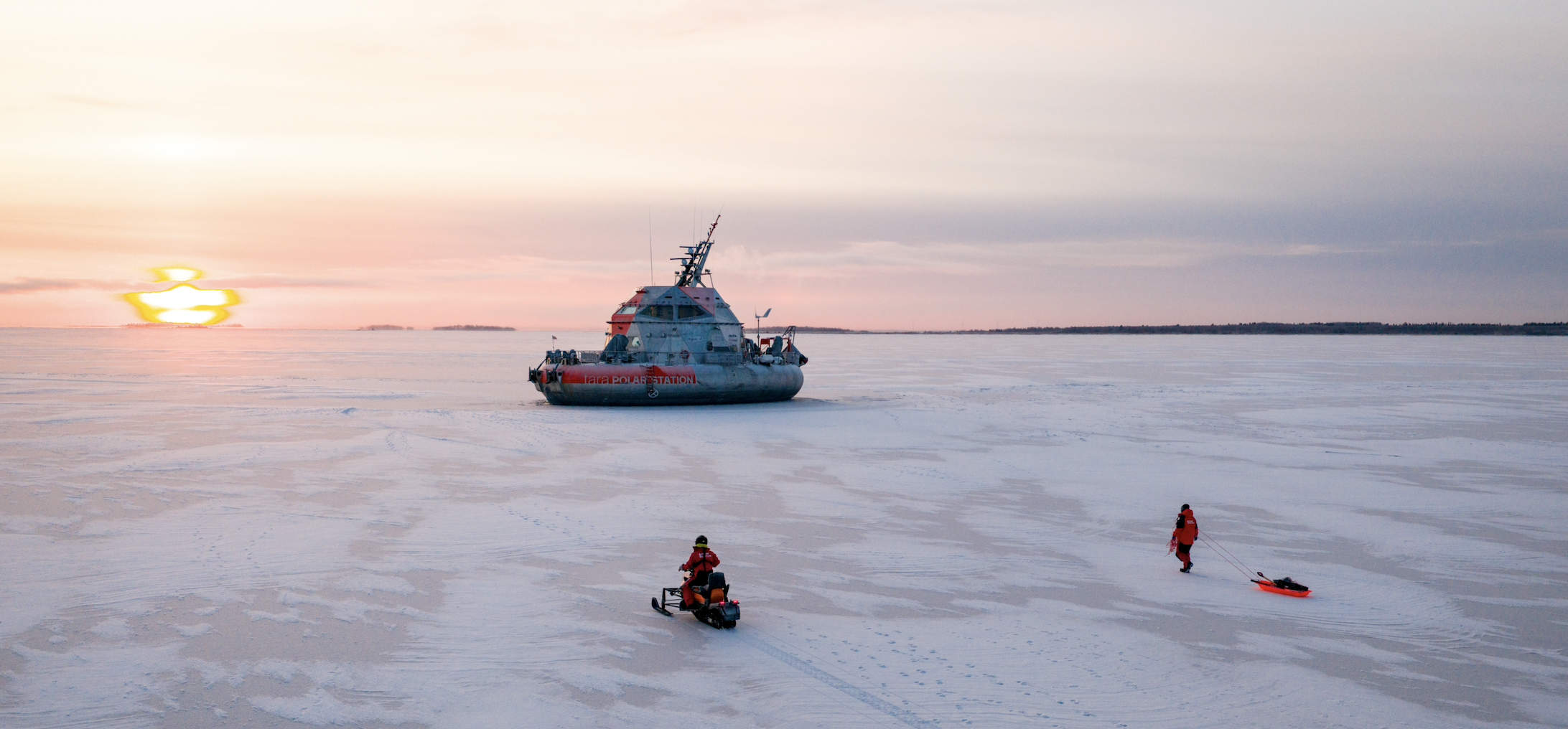 Un navire et des personnes sur la glace au coucher du soleil en Arctique.
