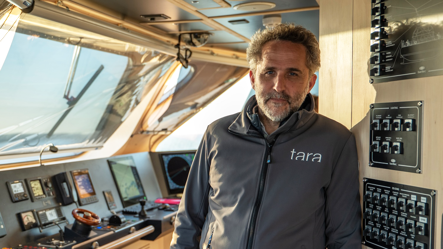 Un homme dans un cockpit de bateau portant une veste avec le logo "Tara".