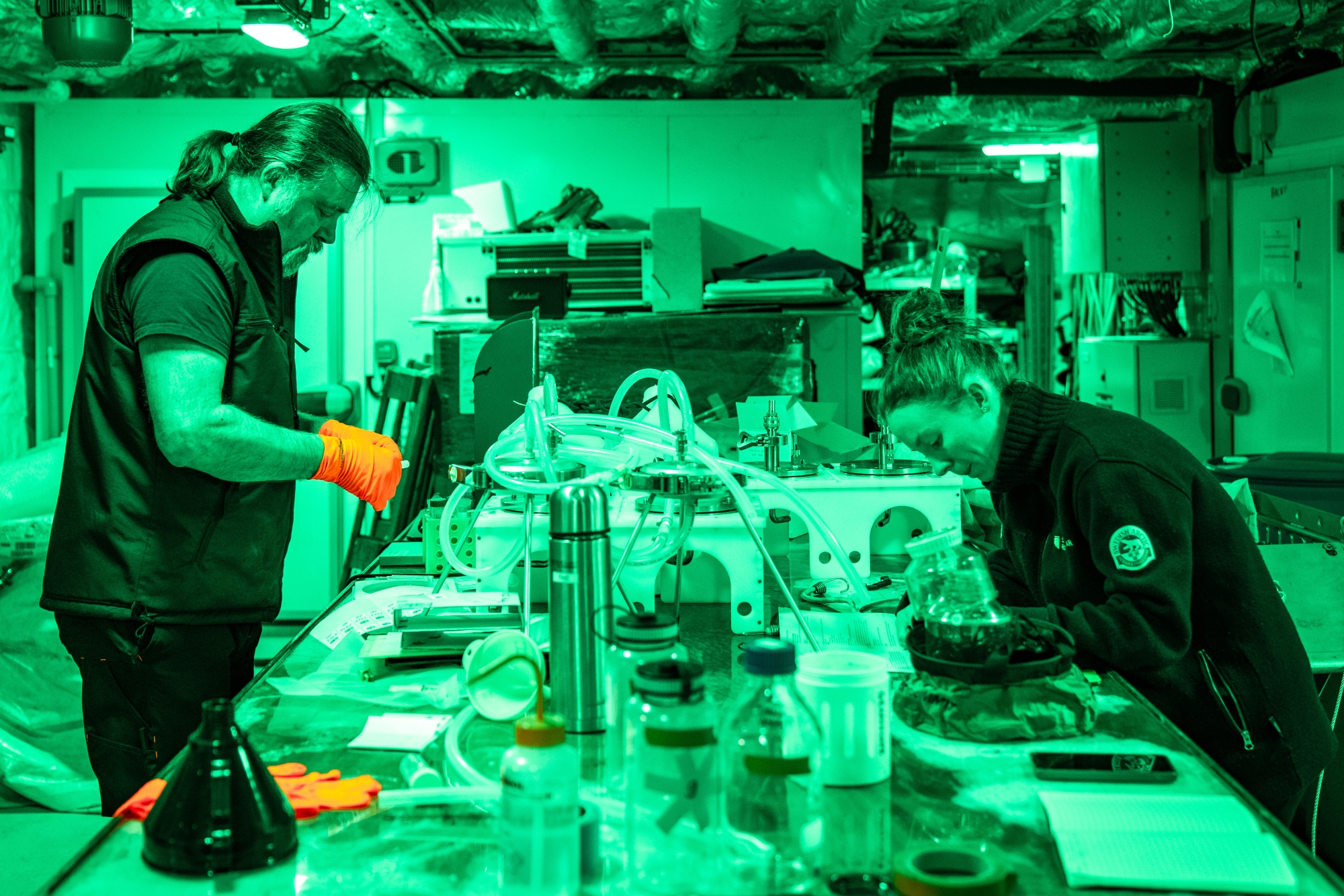 Deux personnes travaillent dans un laboratoire avec des équipements scientifiques sous une lumière verte.