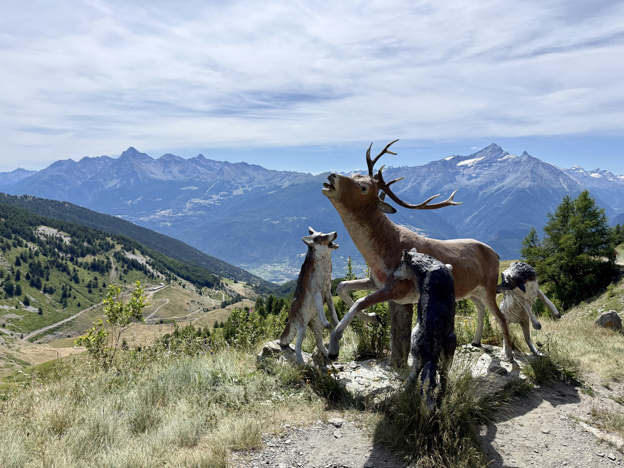 Statues d'animaux dans un paysage de montagne avec des sommets enneigés en arrière-plan.