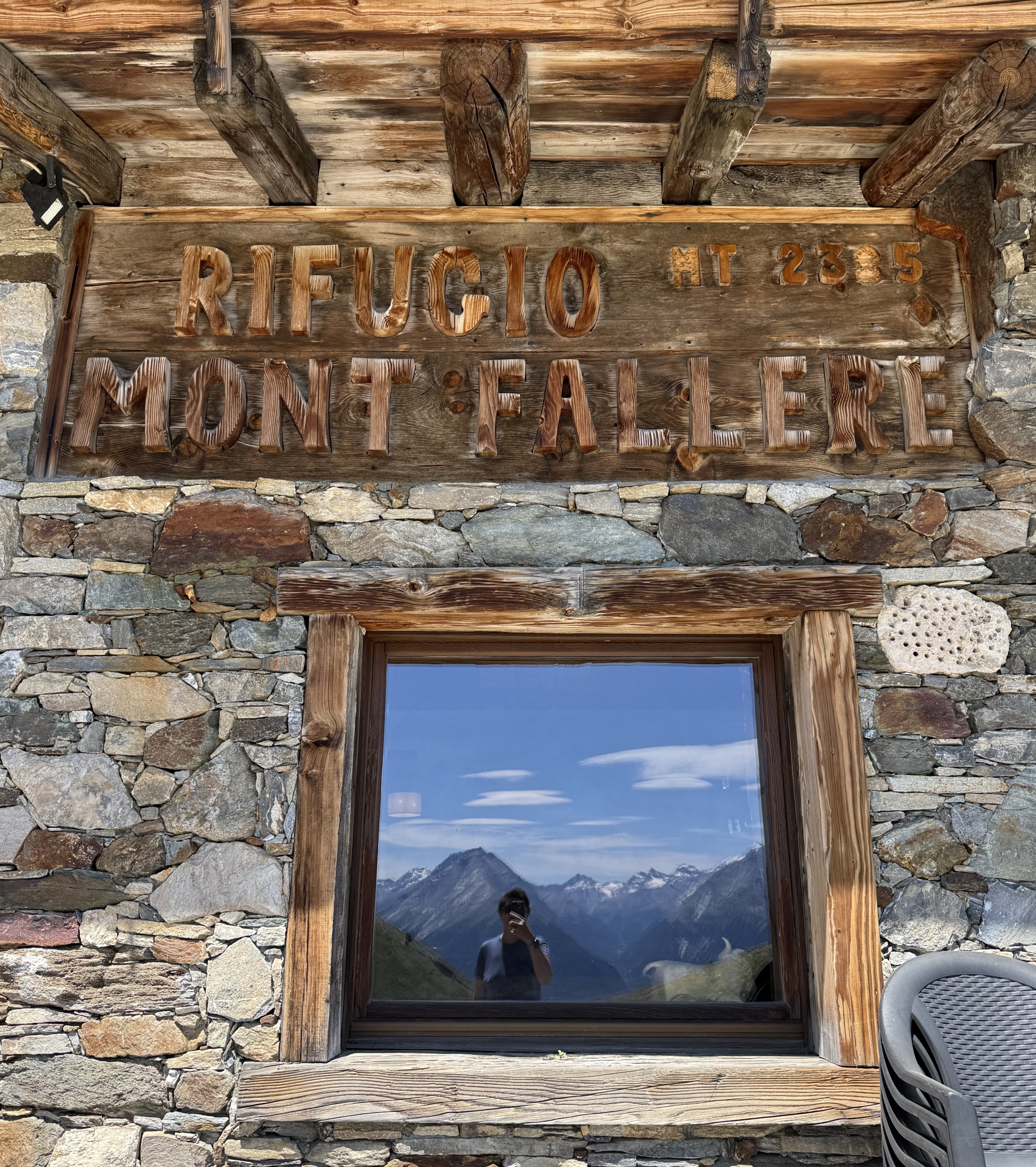 Refuge de montagne Mont Fallère avec fenêtre reflétant un paysage alpin.