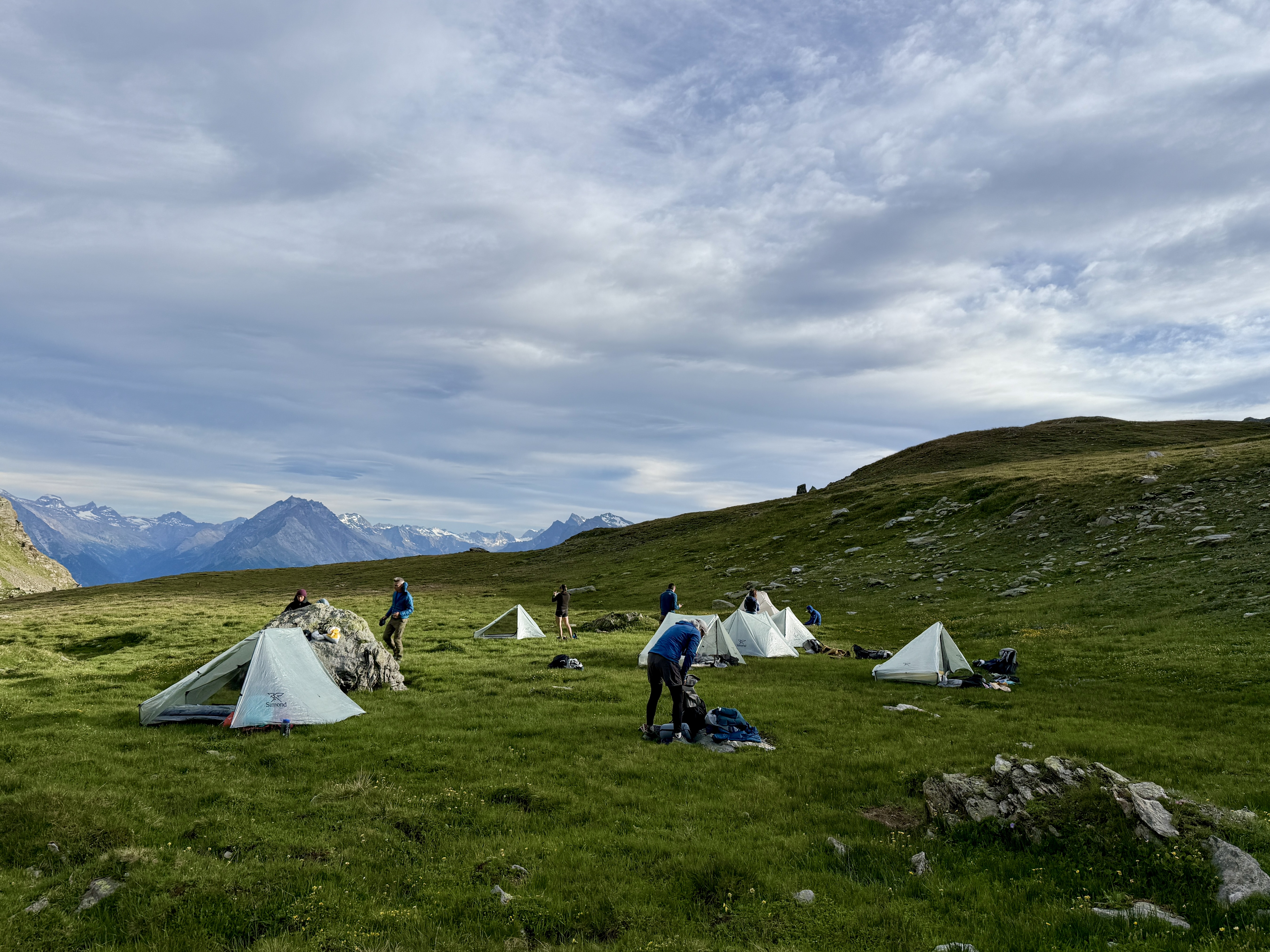 Campement de tentes en montagne avec des randonneurs sous un ciel nuageux.